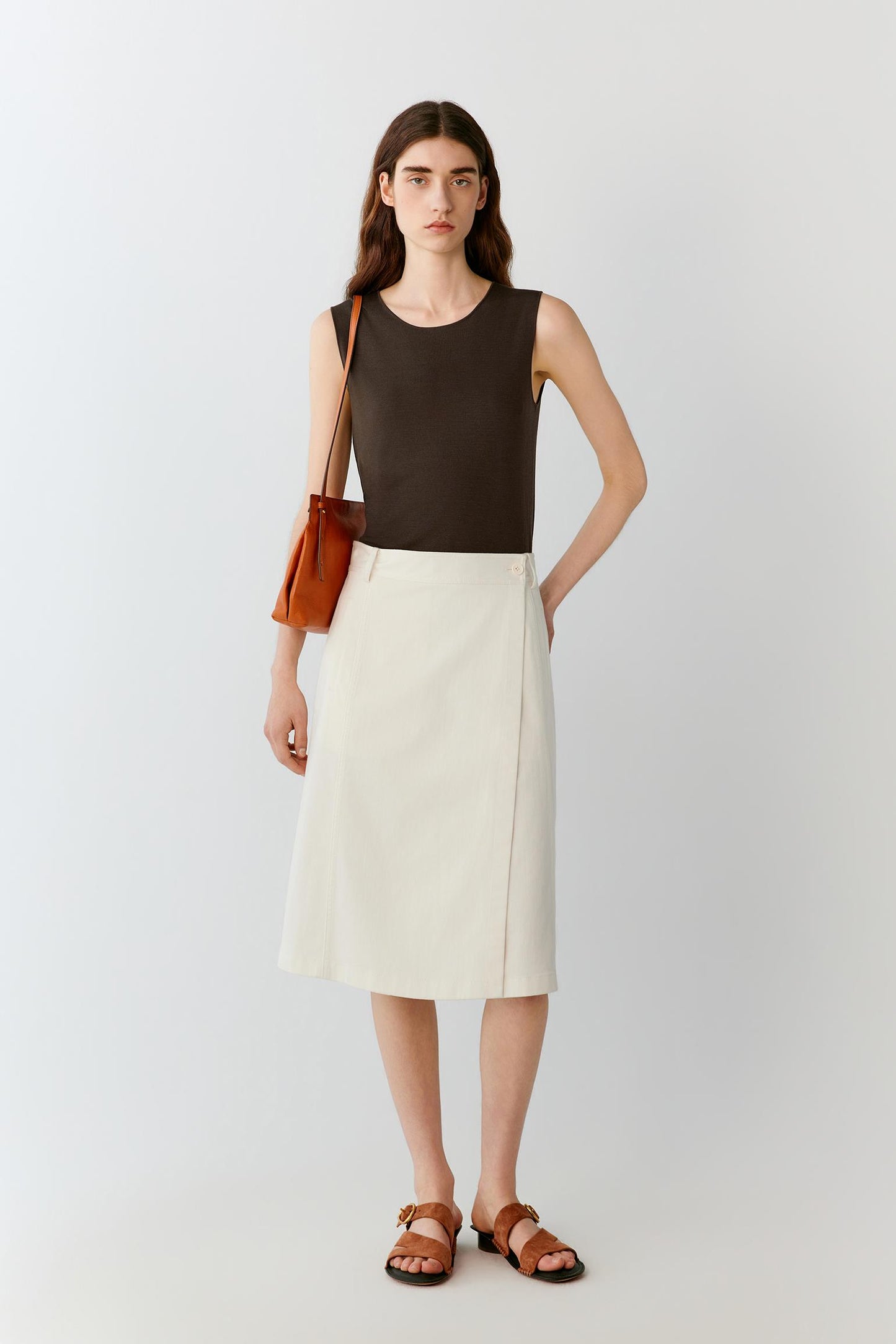 Front view of a woman wearing a dark brown sleeveless top in fine-gauge silk yarn, highlighting the straight silhouette, lightweight knit construction and smooth surface. The round neckline, clean armholes and fluid drape create a refined, minimalist appearance.