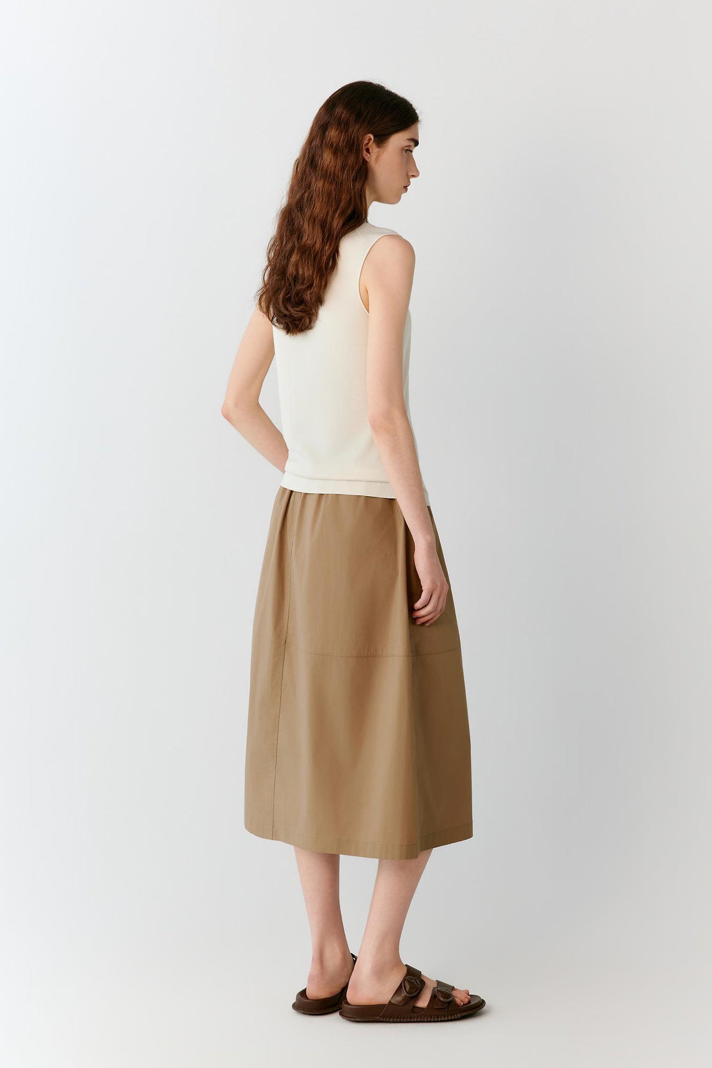 Side view highlighting the fluid drape and softly flared volume of the skirt. The image reveals the clean side construction and the way the lightweight fabric follows the body's movement while maintaining a structured outline.
