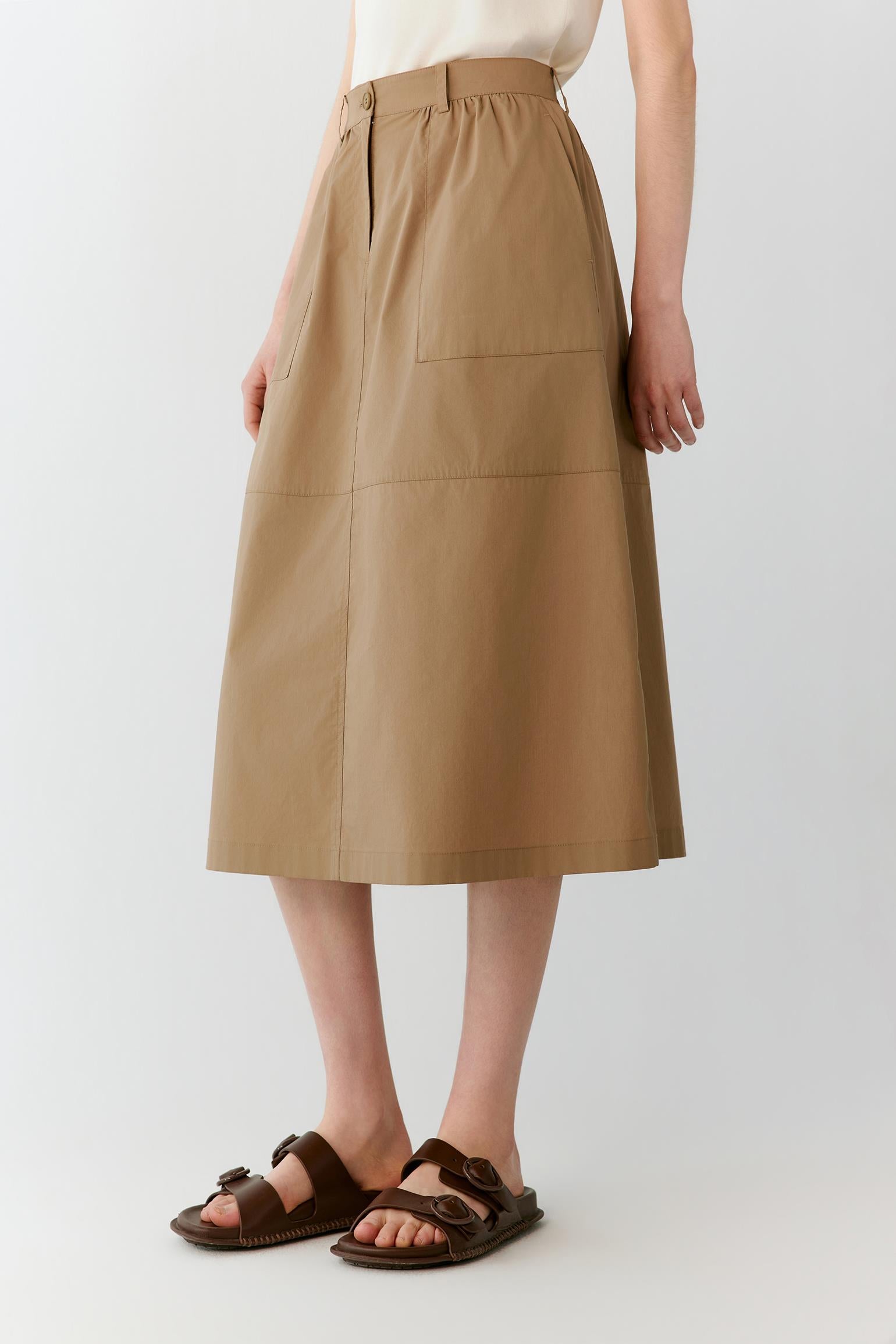 Three-quarter rear view showing the clean panel construction and the fluid fall of the skirt from the fitted waistband. The image emphasizes the balanced silhouette and natural movement of the cotton blend fabric.