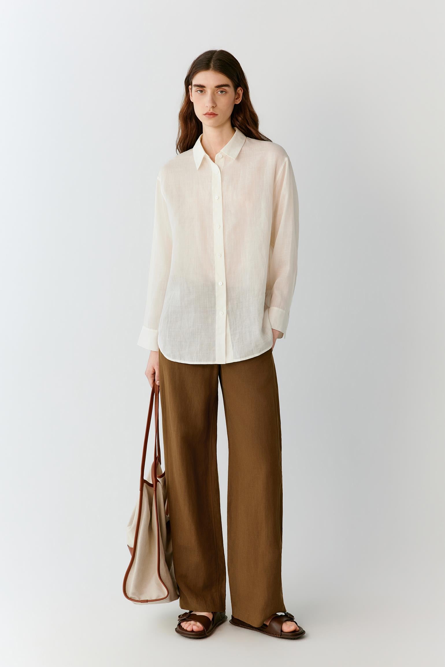 Front view of a woman wearing brown trousers in a silk and linen blend, highlighting the straight-leg silhouette, lightweight construction and fluid drape of the fabric. The clean waistband, front fastening and smooth surface create a refined appearance, while subtle tonal variations add depth to the material.