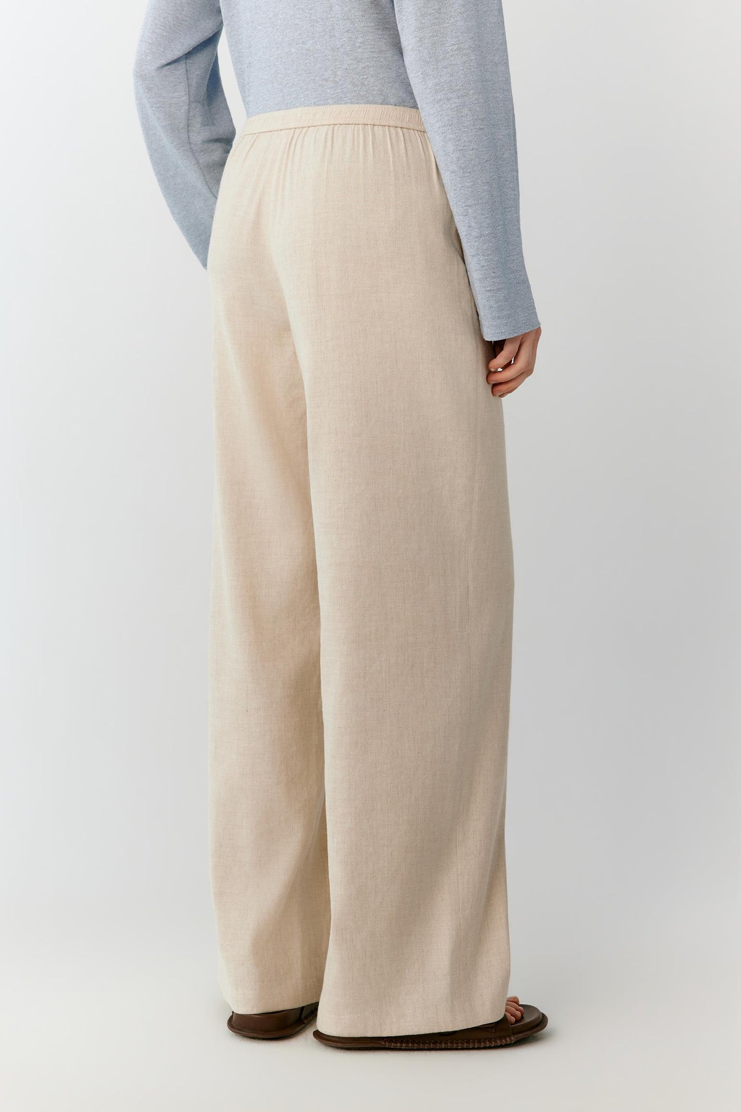 Side view highlighting the straight cut and the way the lightweight linen follows the body's movement. The image reveals the smooth side seam, fluid drape and elongated proportions of the trousers.