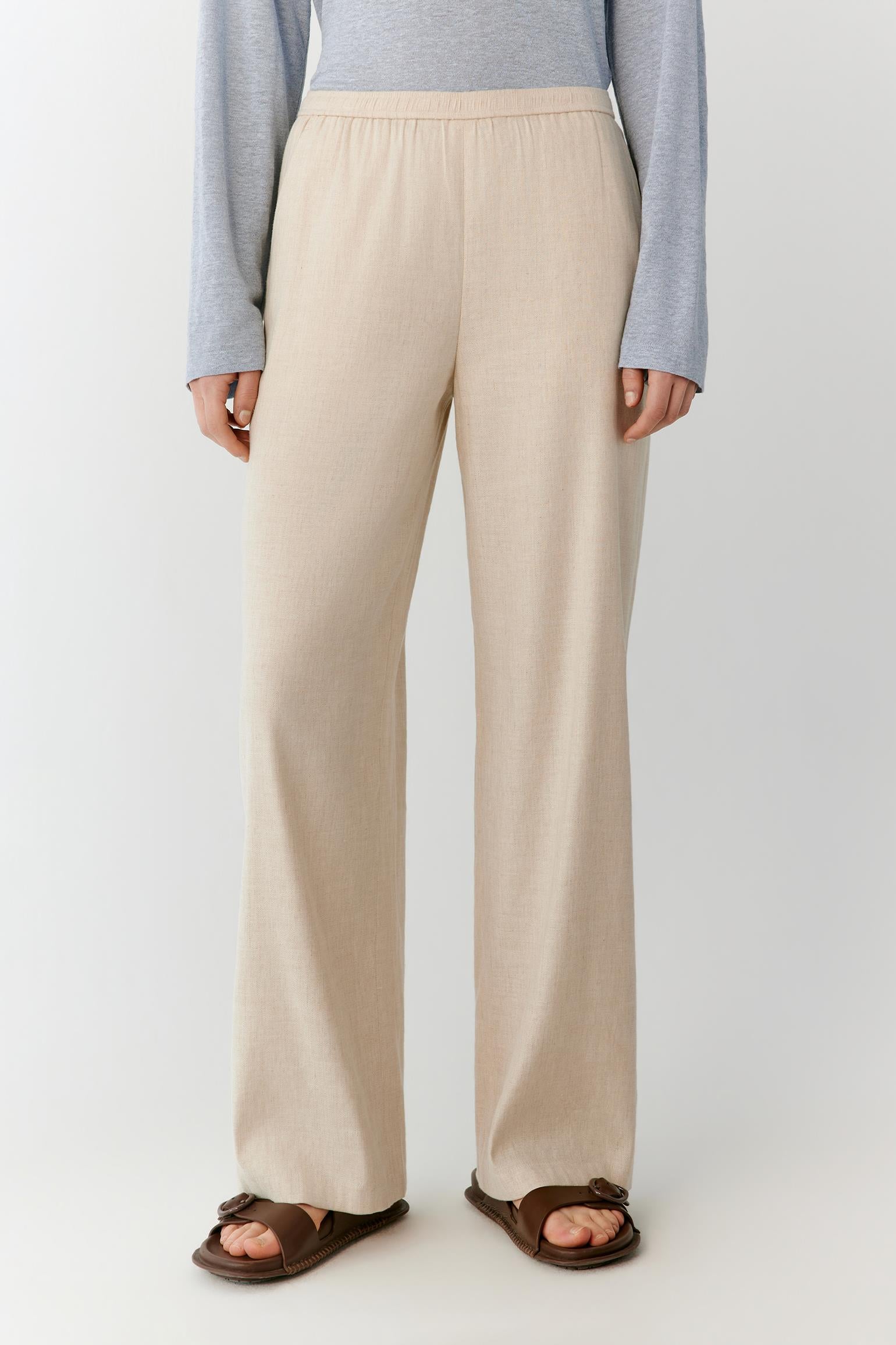 Full-length view focused on the trousers, emphasizing the straight-leg cut, long proportions and soft movement of the lightweight linen fabric. The image highlights the fluid fall from the waistband to the hem and the clean, balanced silhouette.