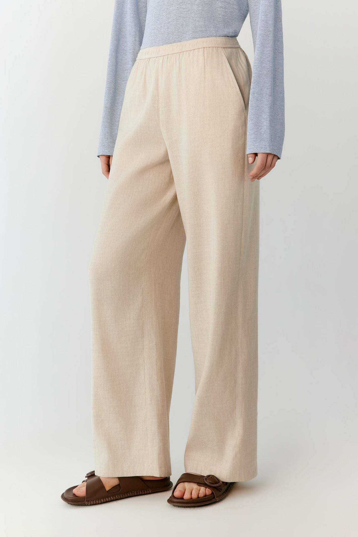 Three-quarter rear view showing the relaxed straight-leg construction and the natural drape of the linen fabric. The image emphasizes the clean back silhouette and the fluid movement of the wide hems.
