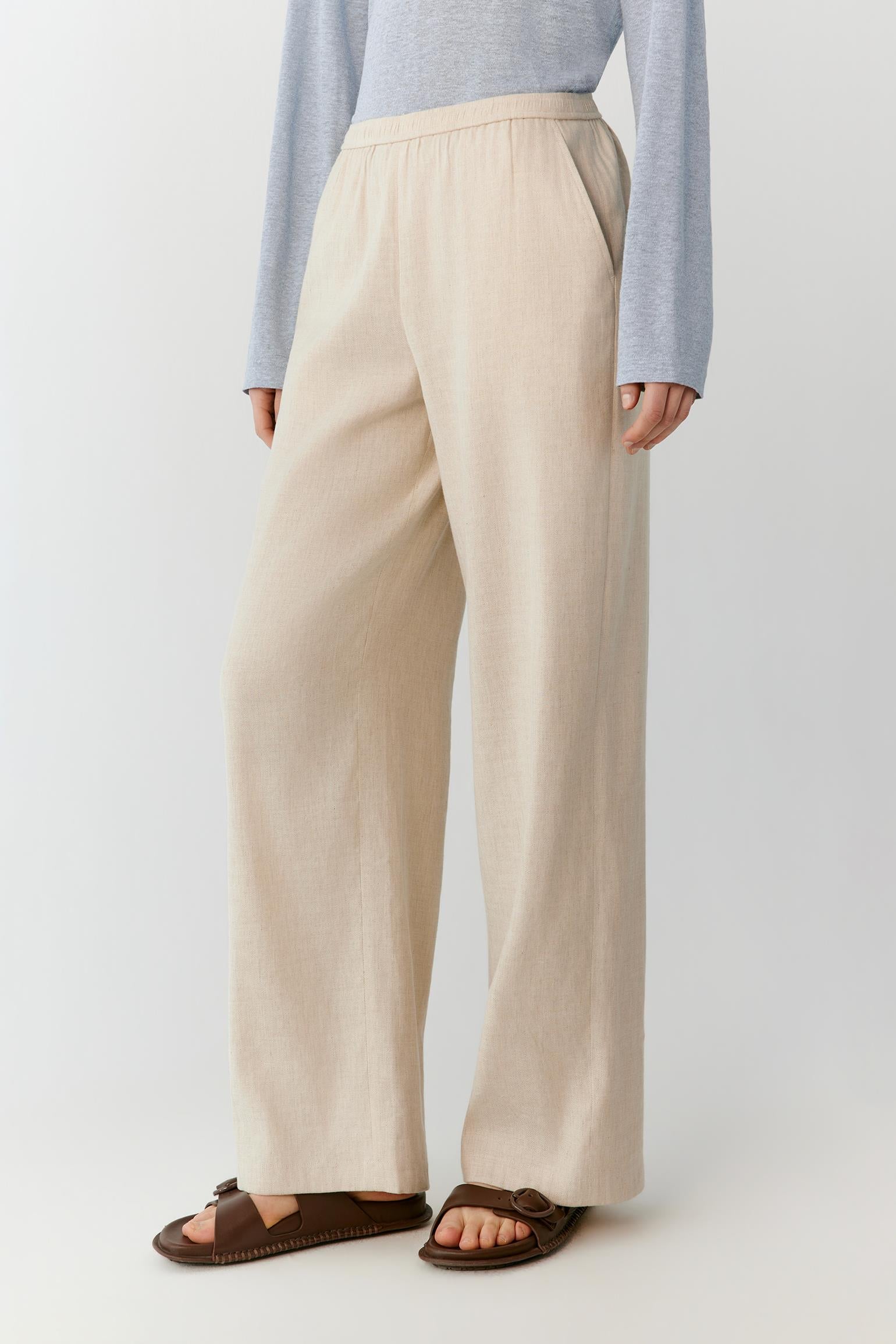 Three-quarter rear view showing the relaxed straight-leg construction and the natural drape of the linen fabric. The image emphasizes the clean back silhouette and the fluid movement of the wide hems.