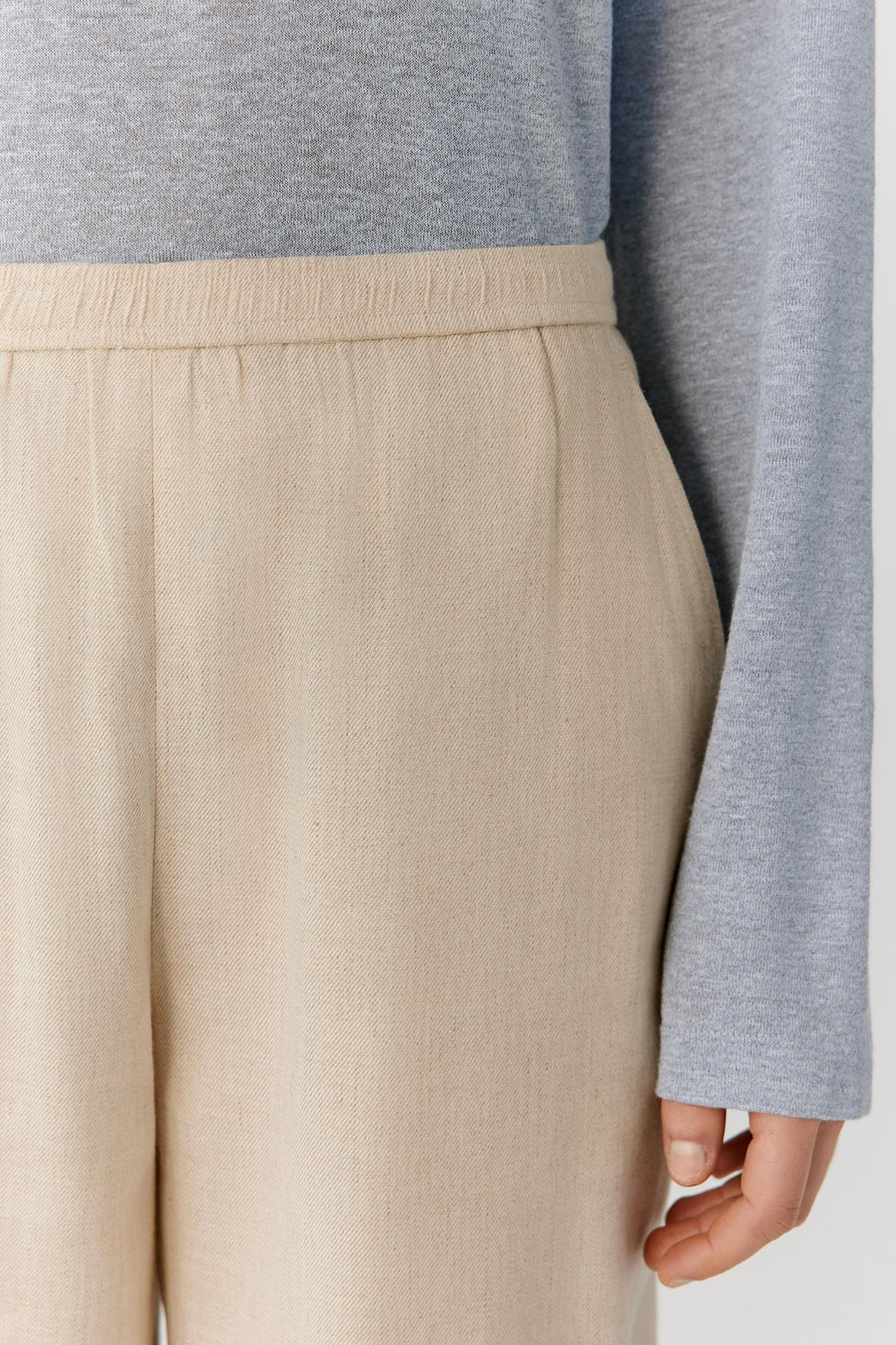 Close-up of the waistband and upper back construction, revealing the clean finishing, natural linen texture and subtle weave. The image highlights the precise tailoring, soft structure and understated appearance of the fabric.