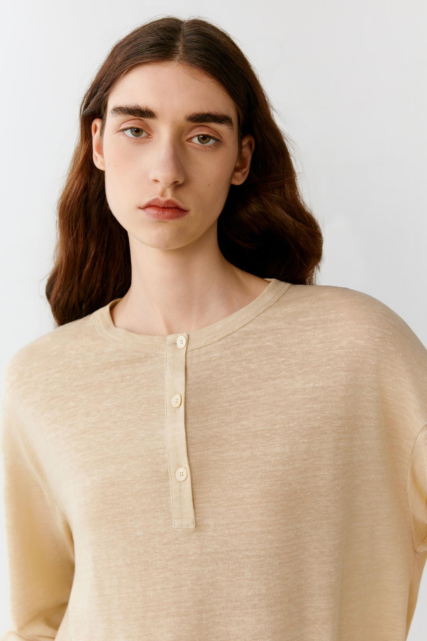 Close-up portrait focusing on the round neckline, dropped shoulders and upper body construction. The image reveals the smooth texture, soft hand and subtle tonal depth of the ivory jersey fabric.