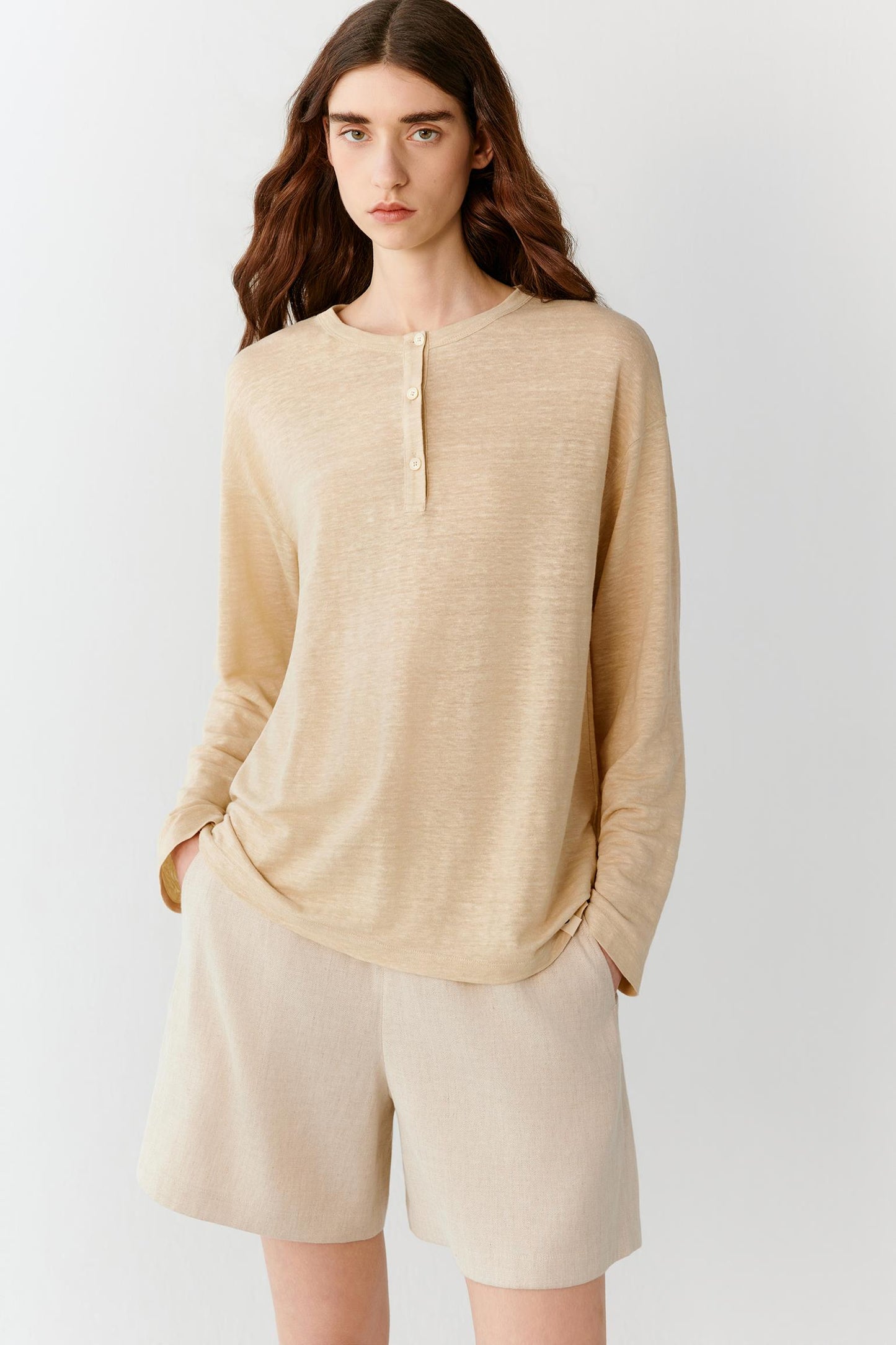 Front view of a woman wearing an ivory top in a linen blend jersey, highlighting the relaxed silhouette, lightweight construction and fluid drape of the fabric. The smooth surface, round neckline and dropped shoulders create a clean, understated appearance.