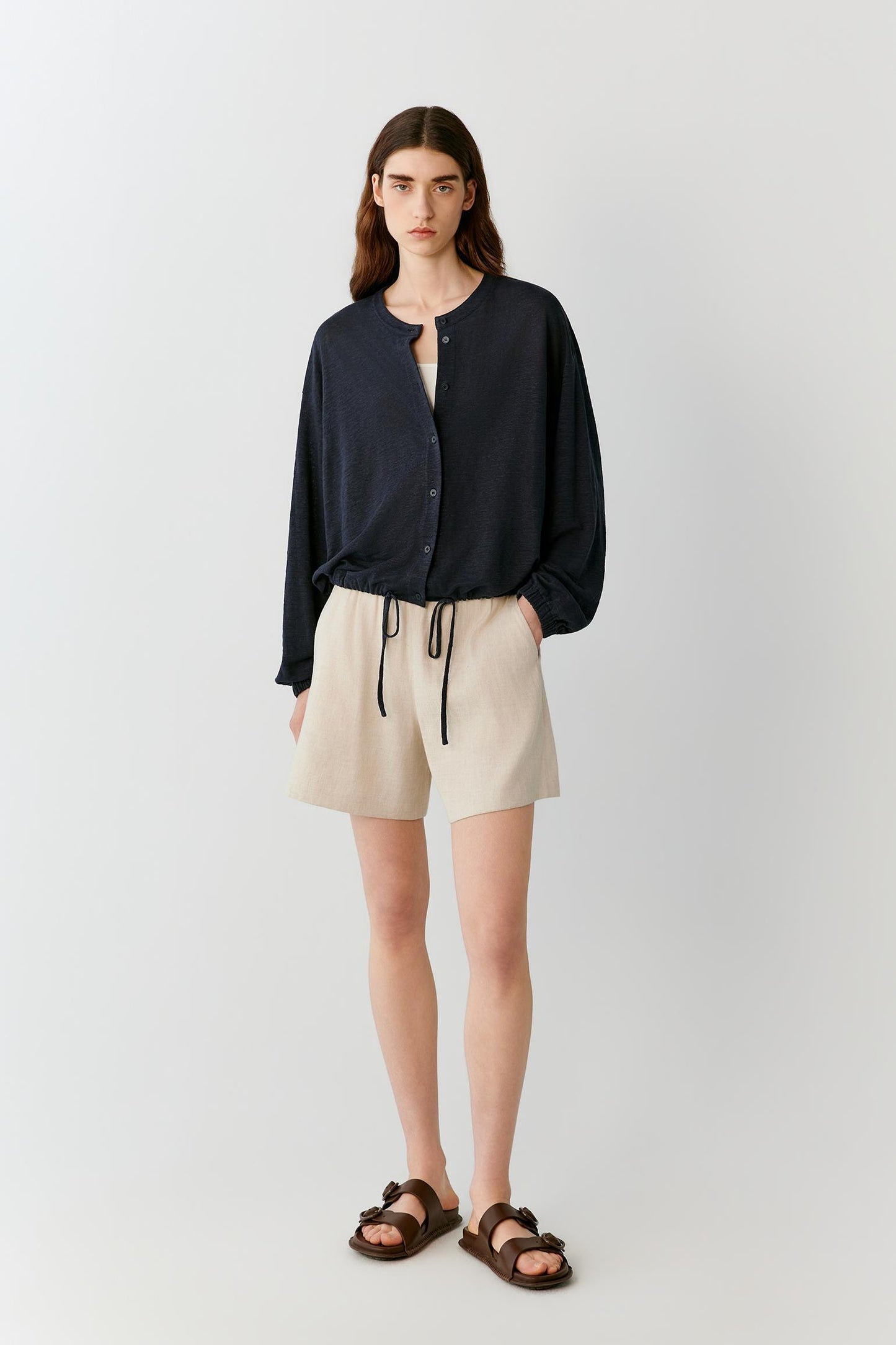 Front view of a woman wearing ivory shorts in a linen and viscose blend, highlighting the relaxed silhouette, lightweight construction and fluid drape of the fabric. The elasticated waistband and clean lines create an effortless, balanced appearance, while the subtle texture of the fabric adds natural depth.