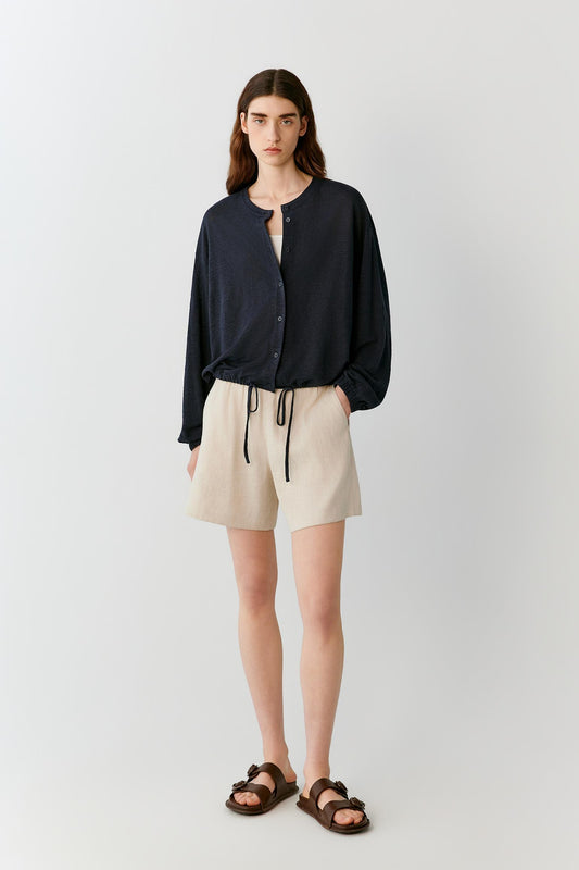 Front view of a woman wearing ivory shorts in a linen and viscose blend, highlighting the relaxed silhouette, lightweight construction and fluid drape of the fabric. The elasticated waistband and clean lines create an effortless, balanced appearance, while the subtle texture of the fabric adds natural depth.