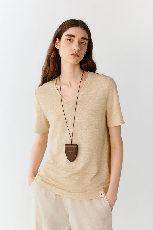 Front view of a woman wearing a light beige top in a linen blend jersey, highlighting the relaxed silhouette, lightweight construction and smooth, softly textured surface. The pointed collar, short sleeves and button-front placket create a casual yet refined appearance, while the fluid fabric falls naturally over the body.