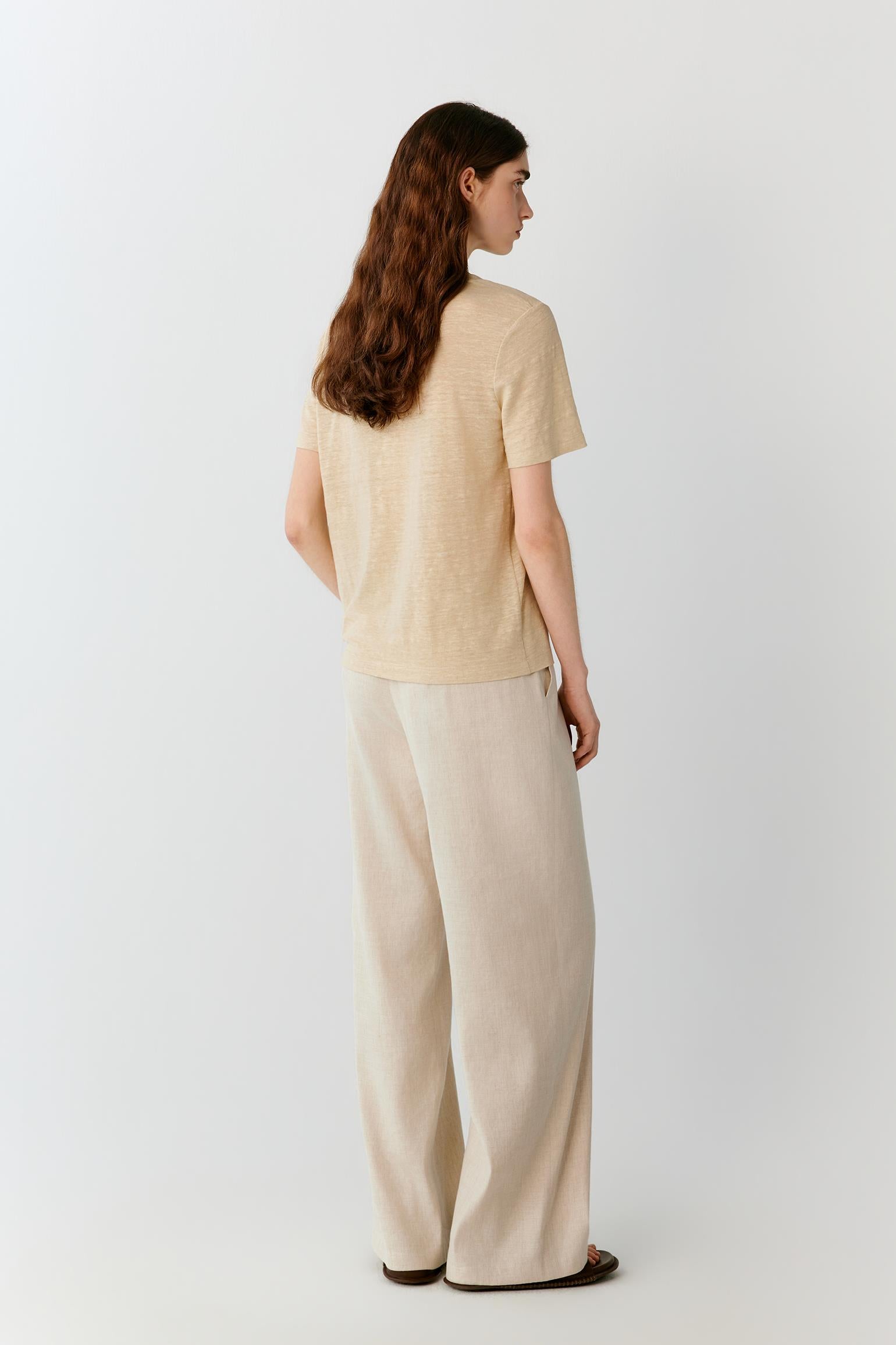 Three-quarter rear view highlighting the clean back construction, relaxed fit and fluid drape of the linen blend jersey. The image emphasizes the natural movement of the fabric and the balanced proportions of the silhouette.