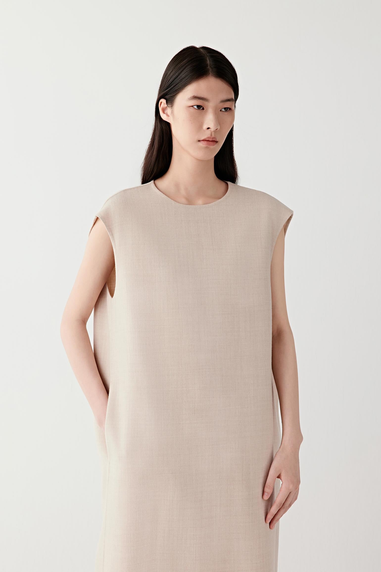 Woman wearing a beige melange lightweight wool dress with a straight, sleeveless cut; mid-length front view highlighting the fluid drape, clean lines and soft structure through the body.