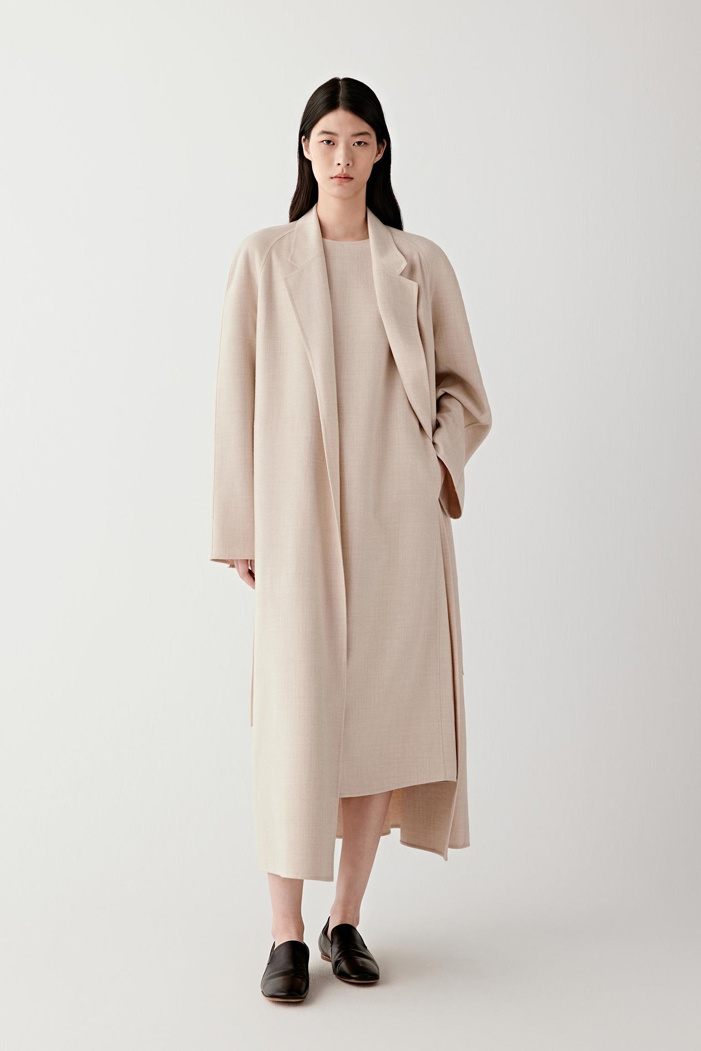 Woman wearing a long beige lightweight wool coat, front view with relaxed fit.