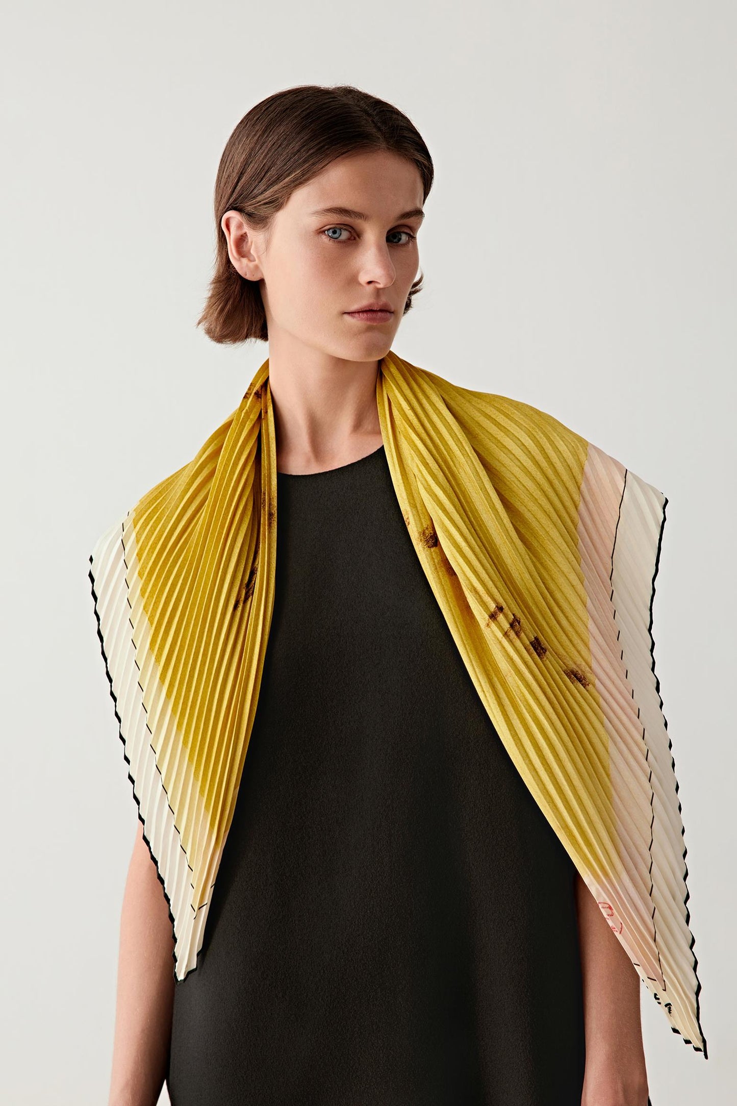 Woman wearing a yellow silk twill scarf draped over a sleeveless black dress, front view.