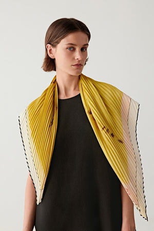 Front view of a model wearing a silk twill scarf featuring the artwork Sphinx (2024) by French artist LOLA. The scarf is draped around the shoulders, revealing a luminous yellow ground with graphic black lines.