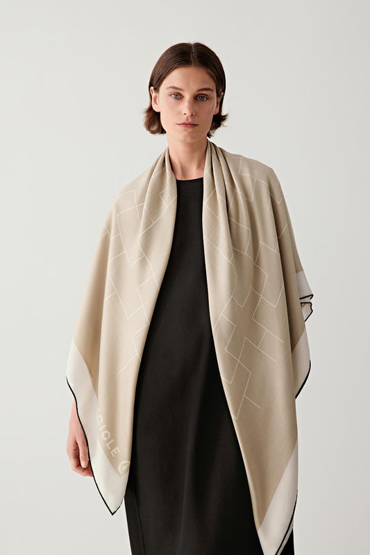 Model wearing a large cashmere and silk scarf in a soft beige tone, draped over the shoulders to show its fluid silhouette and lightweight texture.