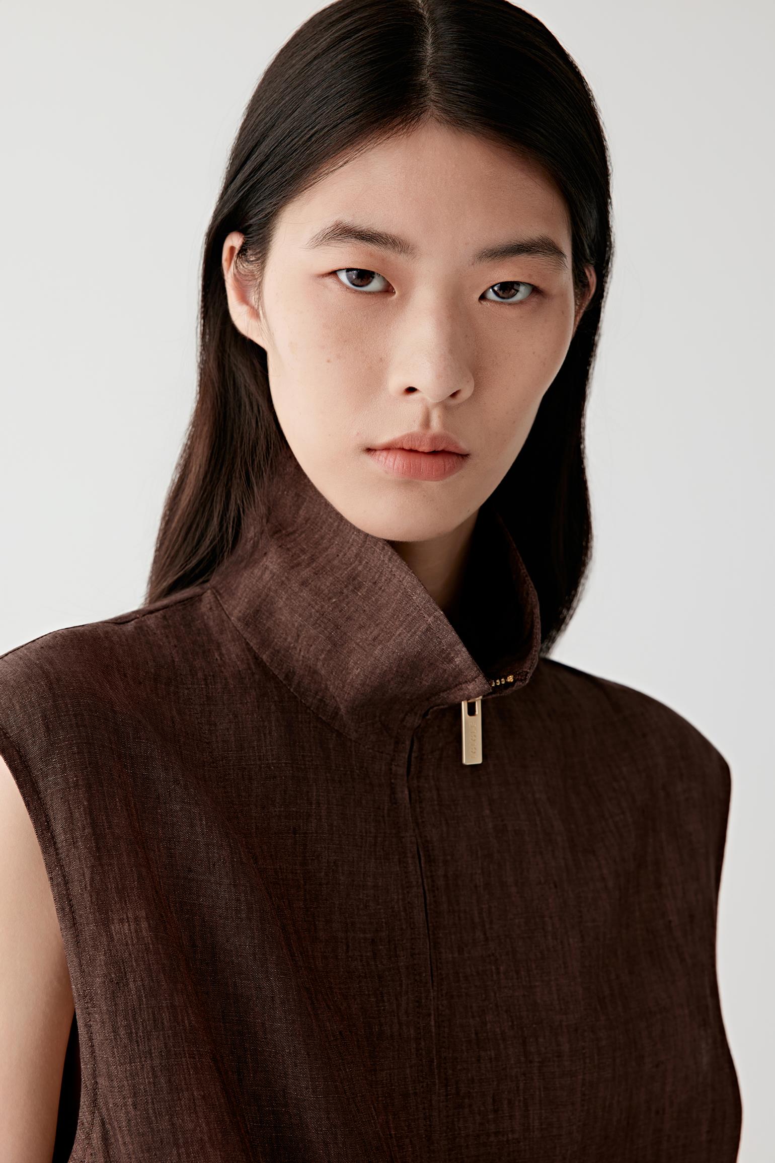 Close-up portrait focusing on the neckline and zip detail, showing hardware, stitching and the slightly textured linen surface