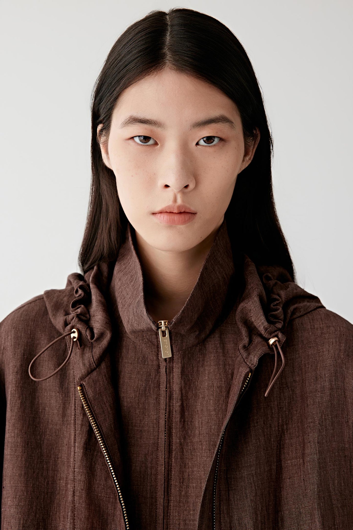 Close-up portrait focusing on the hood and neckline, showing seam construction, edge finishing and the slightly irregular texture characteristic of linen fibres