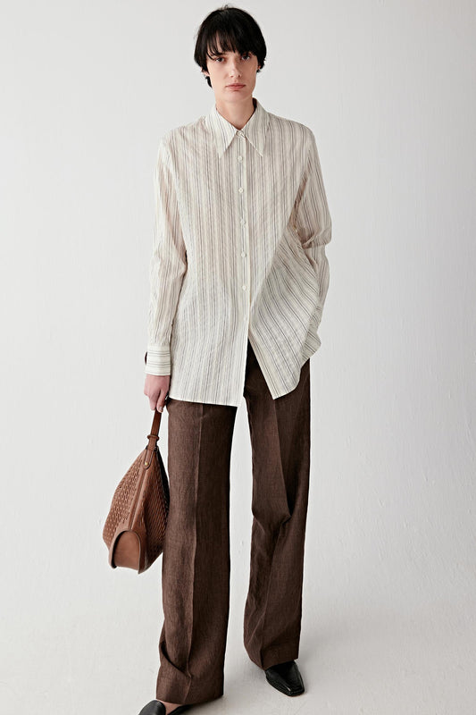 Full-length front view of a woman standing facing forward wearing brown straight-leg linen trousers styled with a light, loose shirt, showing a clean silhouette, straight cut from hip to ankle and a softly structured drape