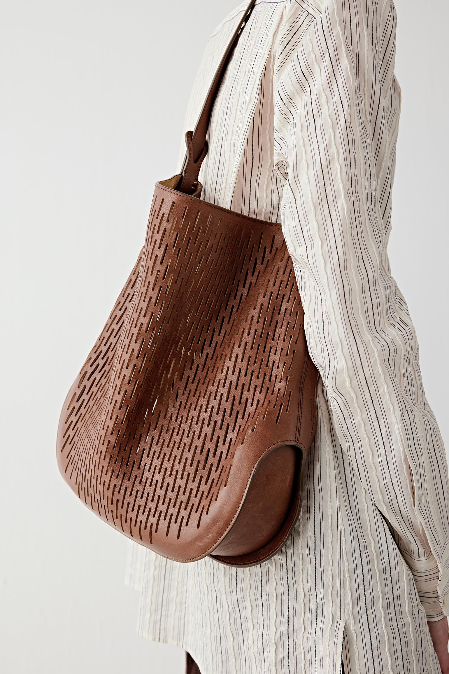 Close-up of the perforated dark brown leather surface and shoulder strap, highlighting the texture, graphic pattern and soft construction.