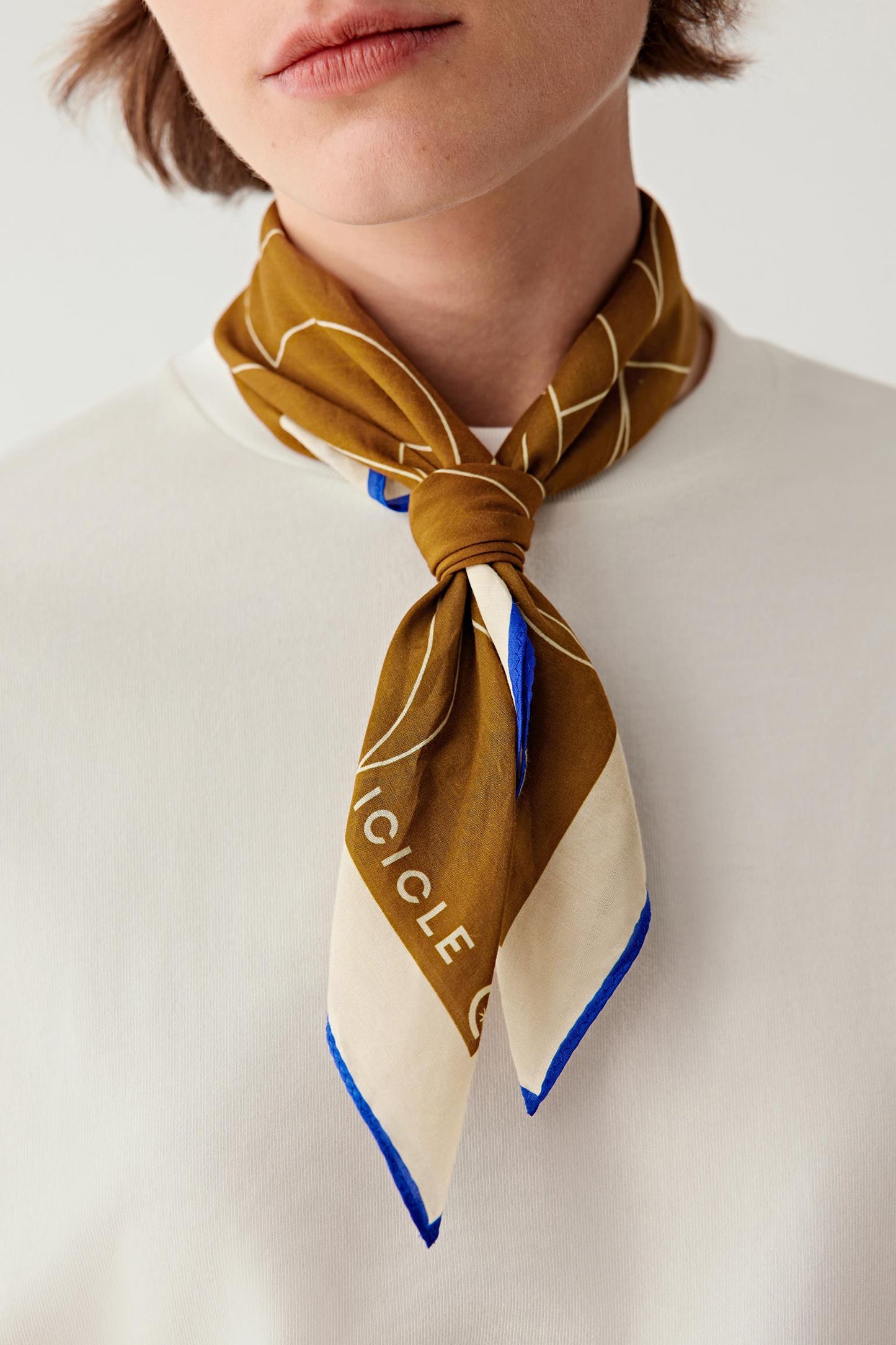 Person wearing a mustard yellow scarf with blue border and 'Ciclo' branding on a white background