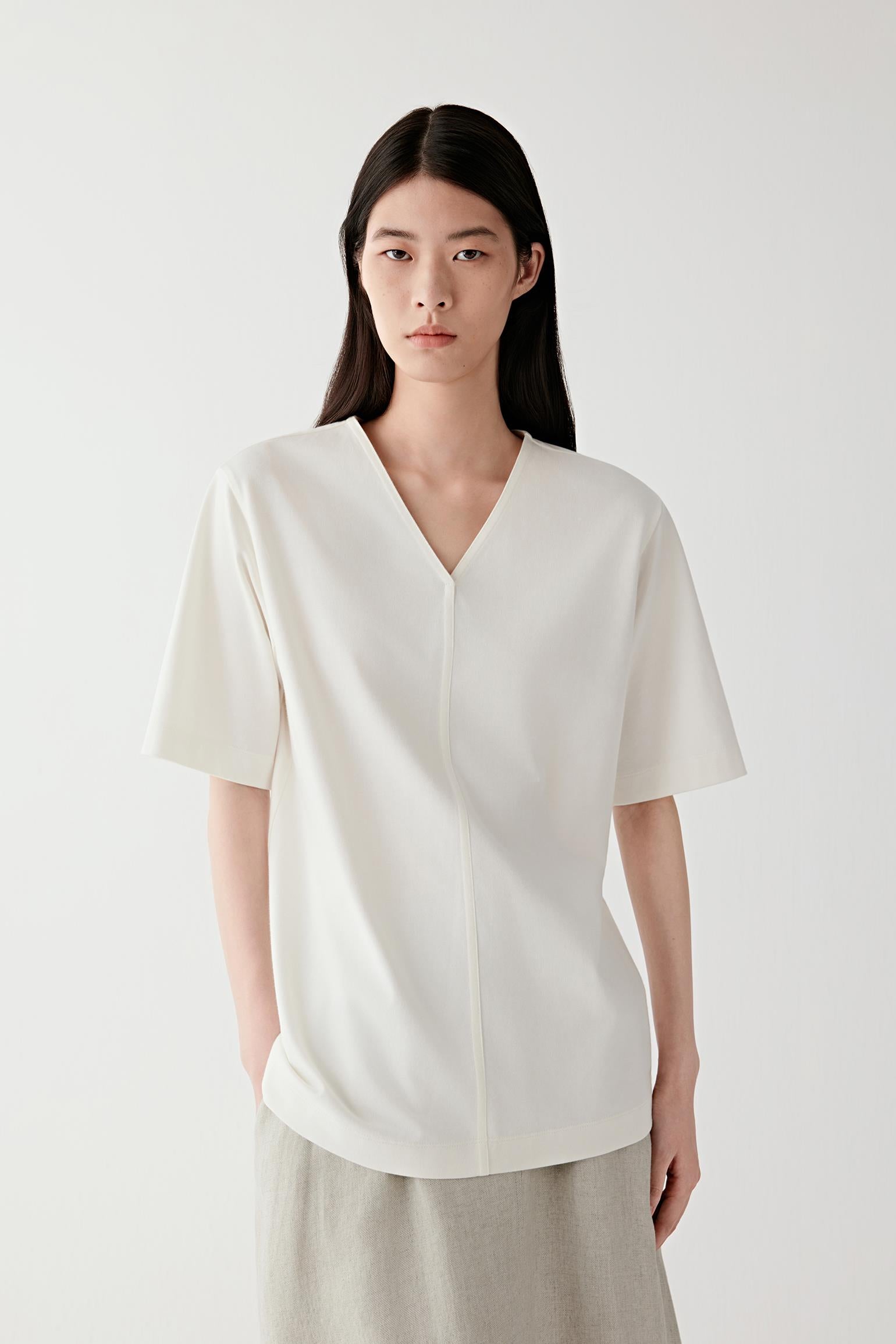 Front view of a woman wearing a cream T-shirt in cotton jersey, highlighting the smooth surface, soft hand and lightweight structure of the fabric. The matte jersey surface reveals a clean and minimal appearance.