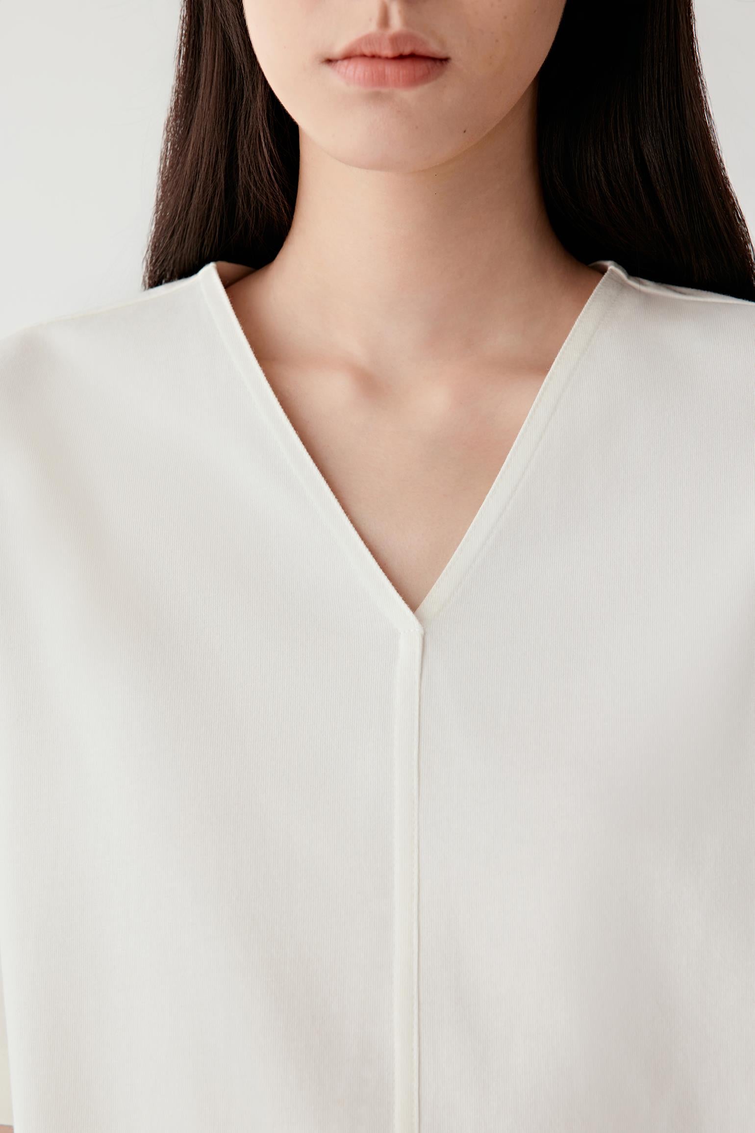 Close-up portrait focusing on the V-shaped neckline and central seam construction, detailing the smooth jersey texture and soft matte finish of the cream shade.
