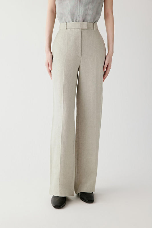 Front view of a woman wearing beige-grey trousers in linen twill, highlighting the dry textured surface, visible grain and softly structured drape of the fabric. The twill weave introduces subtle tonal variation and a matte appearance.