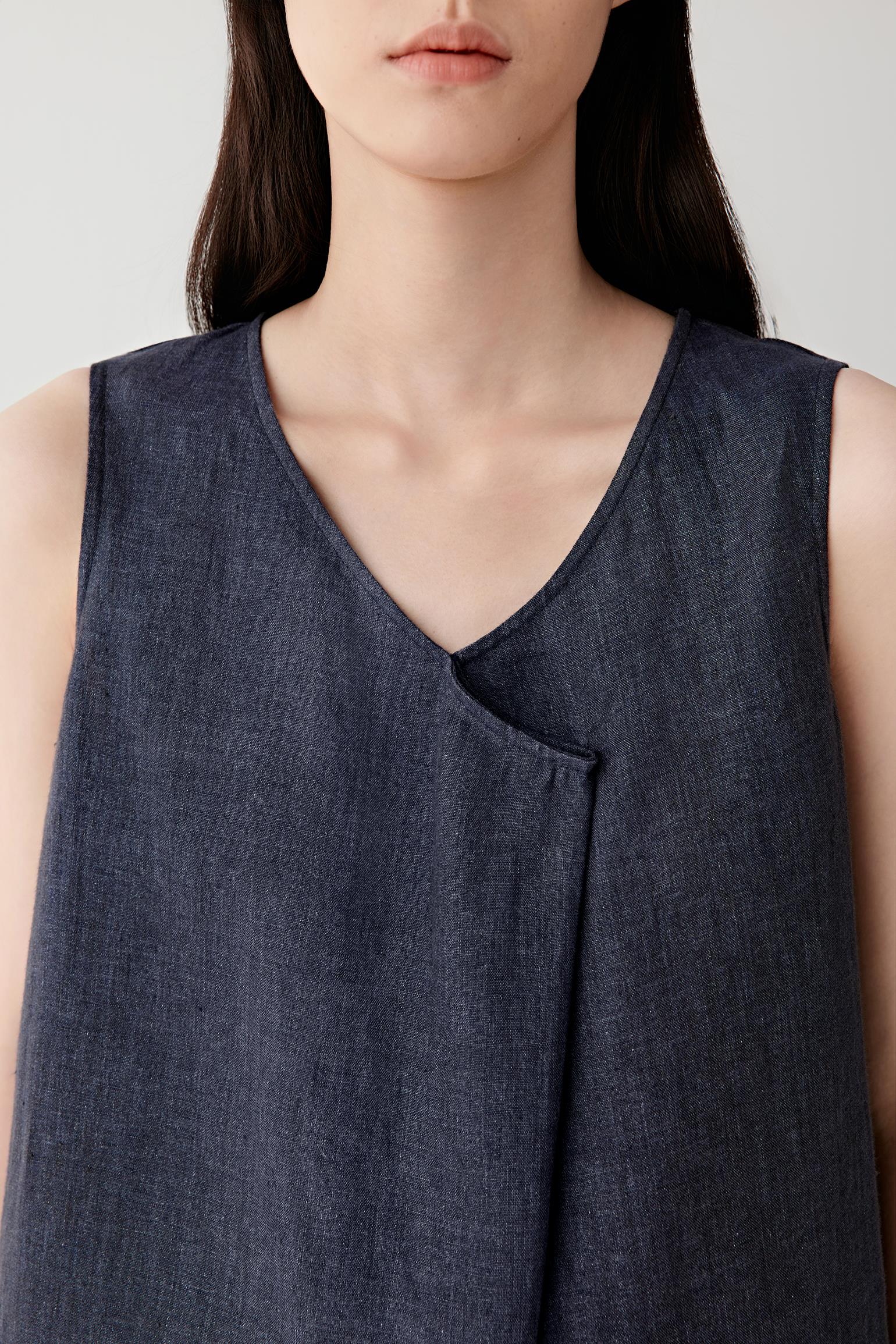 Close-up portrait focusing on the V-shaped neckline and overlapping front panel detailing, revealing the dry woven texture and subtle tonal irregularities of the linen fabric.
