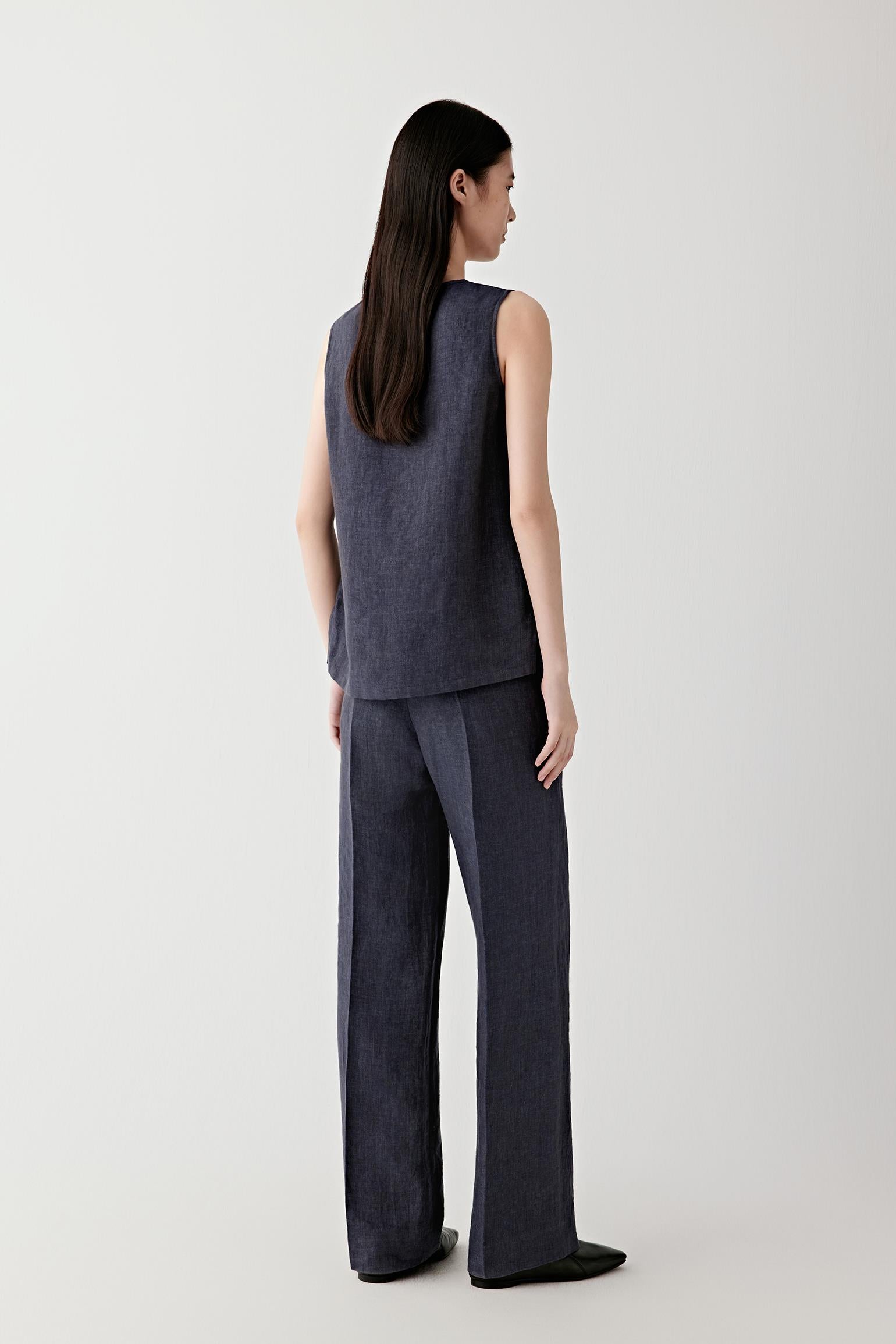 Side or back view emphasizing the fluid drape and layered construction of the blouse. The natural linen texture introduces depth and movement across the indigo blue surface.