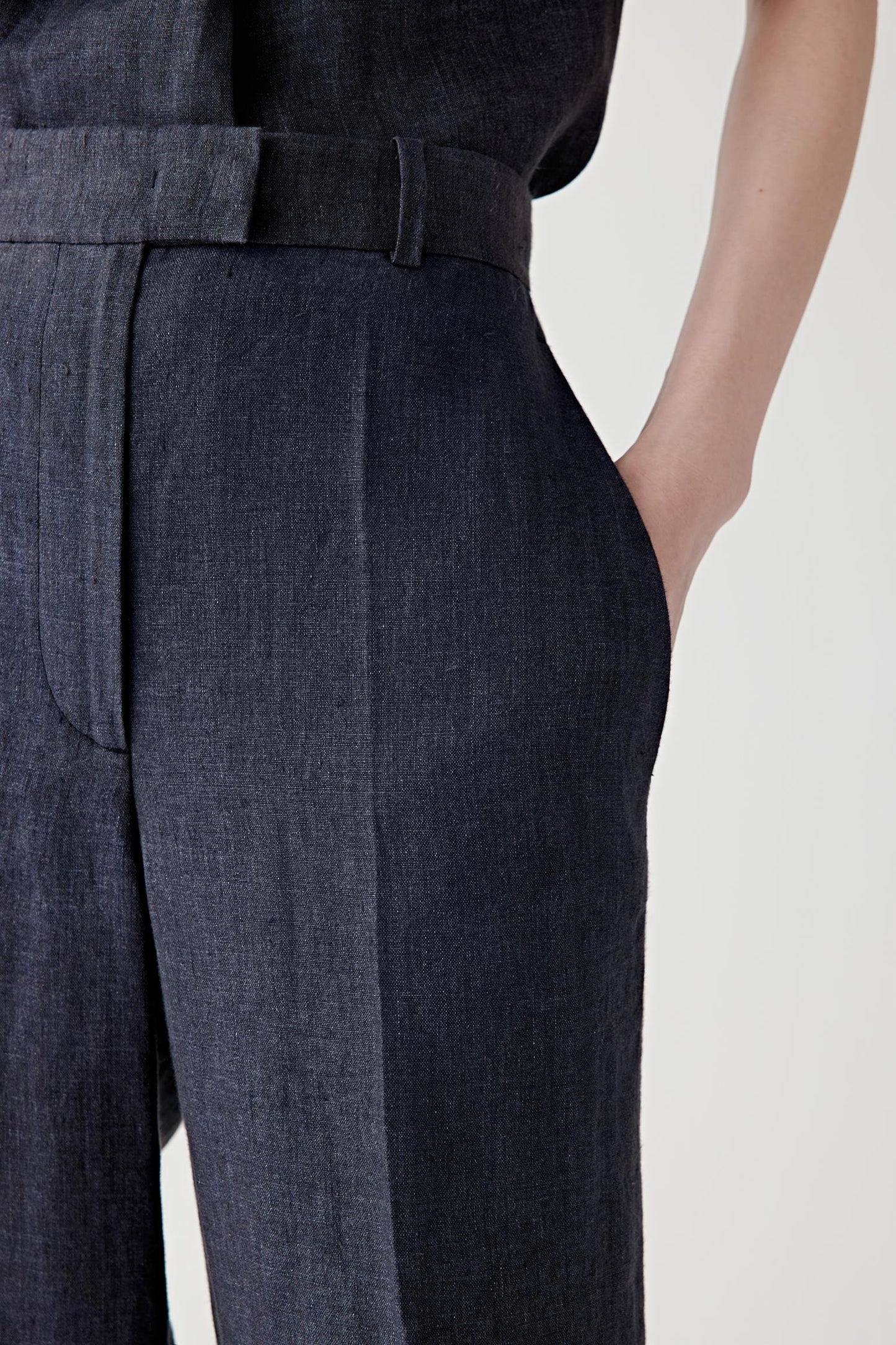 Close-up of the waistband and pleat construction detailing the front pleats, clean finishing and discreet pocket construction. The matte linen surface reveals subtle tonal variation.