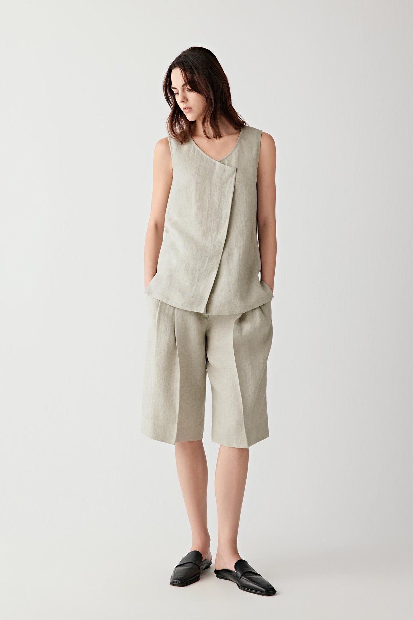 Full-length front view showing the sleeveless silhouette, V-shaped neckline and overlapping front panel construction. Side slits introduce movement and fluidity through the elongated silhouette.