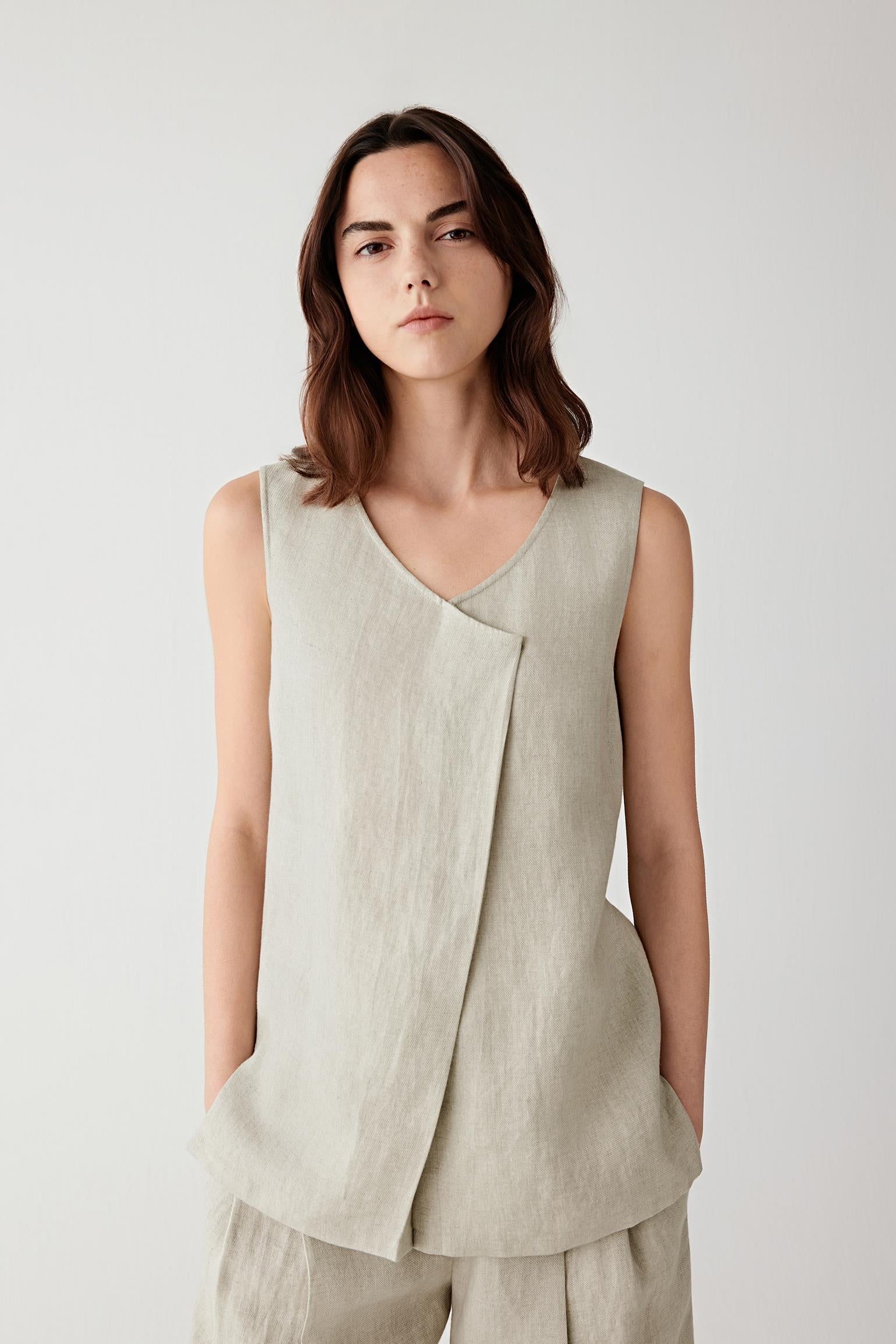 Front view of a woman wearing a beige-grey top in linen twill, highlighting the dry textured surface, visible grain and lightweight structure of the woven fabric. The material falls softly while maintaining gentle structure.