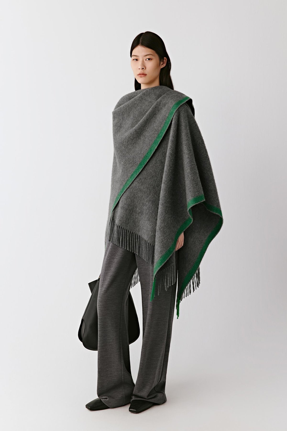 Front view of a woman wearing a grey cashmere shawl with contrasting green edges and fringed trims.