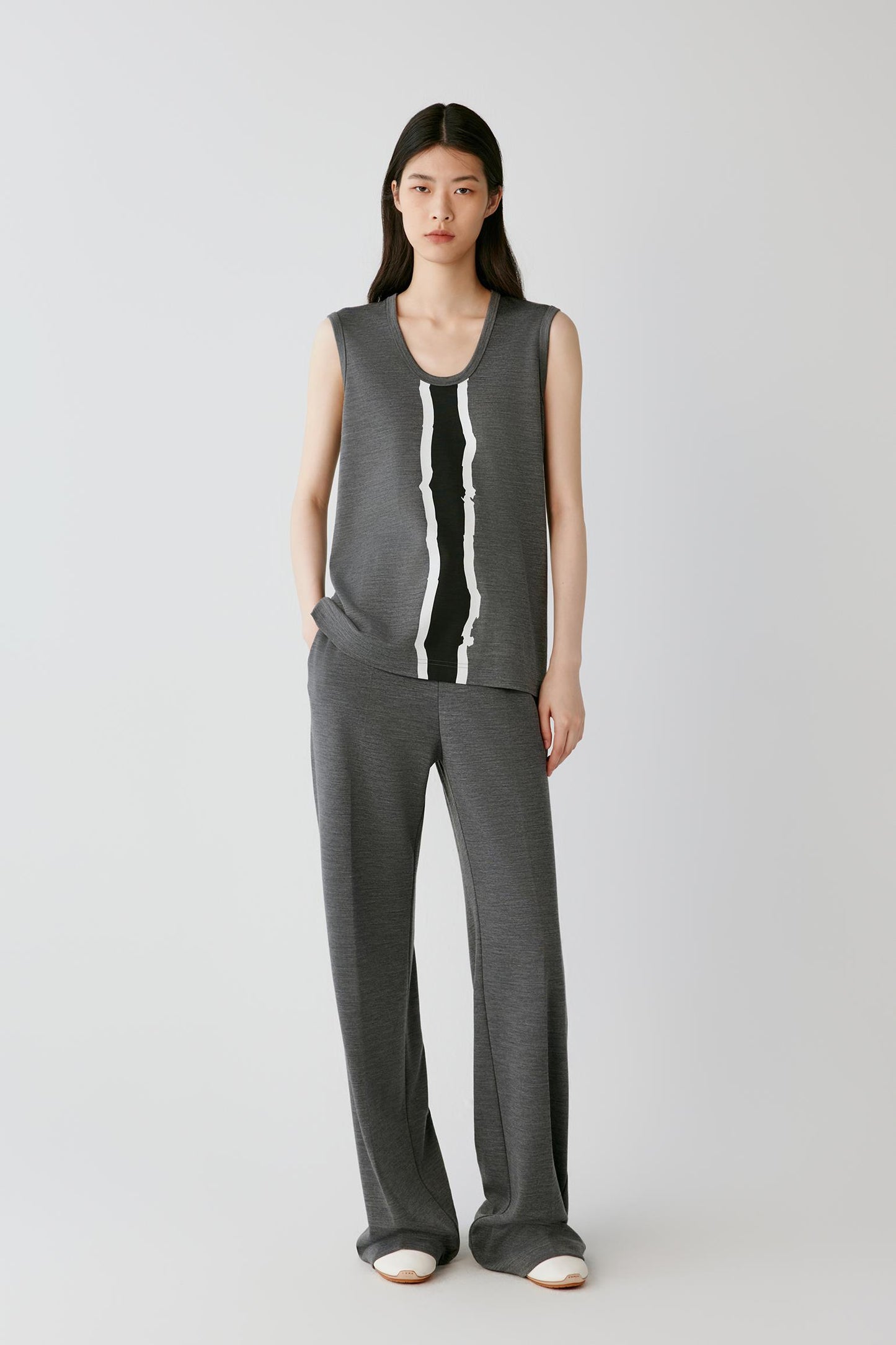 A model stands against a light gray studio background wearing a dark gray sleeveless knit top with a vertical black and white stripe detail, paired with matching dark gray wide-leg knit pants.