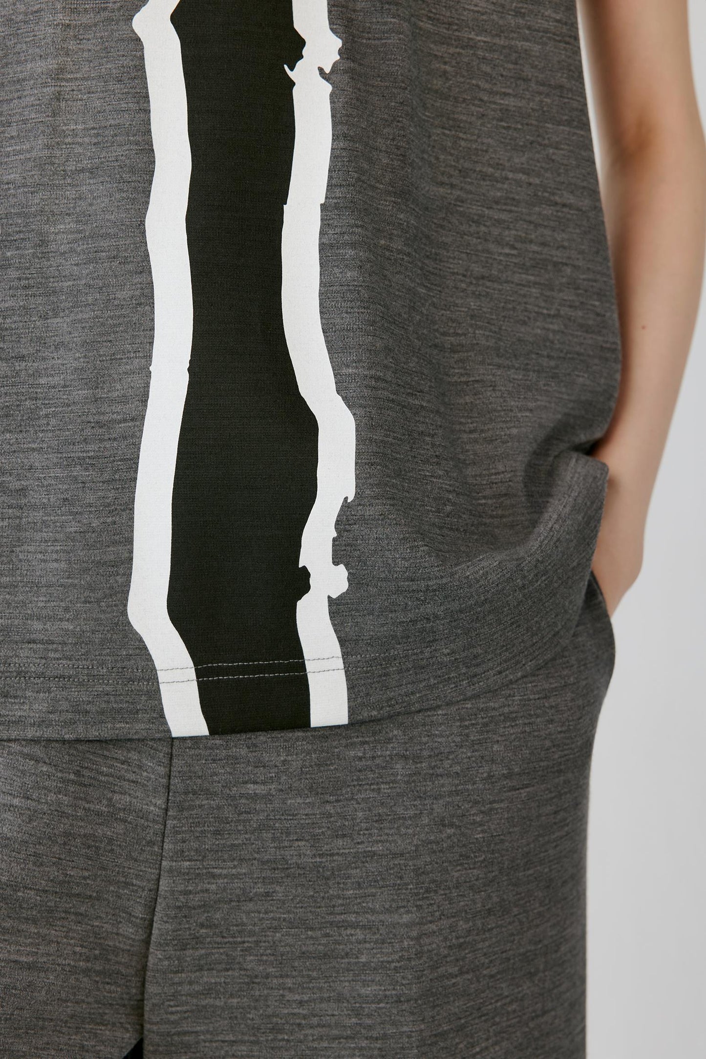Close-up of a heather gray sleeveless top or dress with a bold vertical black and white graphic stripe, shown on a model with a hand in the pocket.