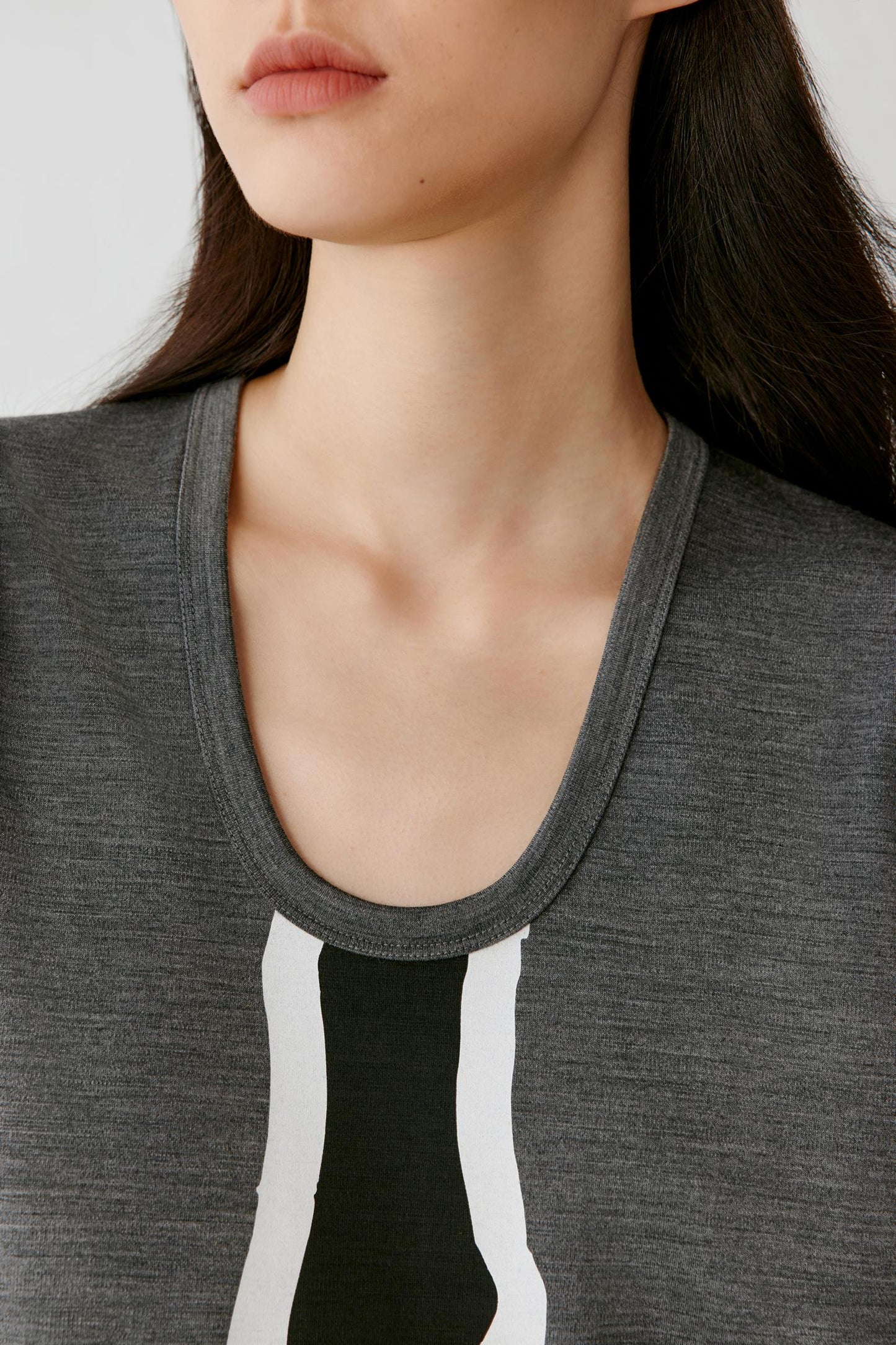 Close-up of a model wearing a dark gray scoop-neck top with a graphic print featuring vertical white and black stripes.