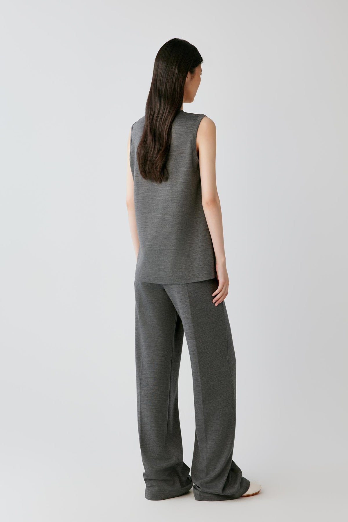 A woman shown from the back wearing a dark gray sleeveless knit top and matching wide-leg knit pants against a light gray studio background.
