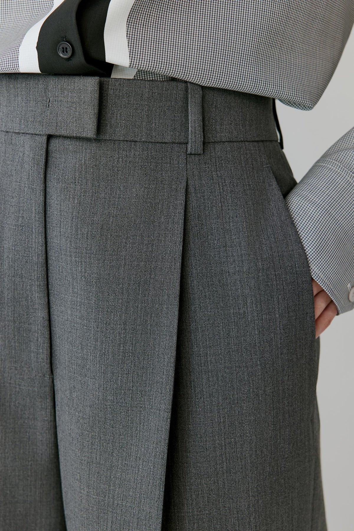 Close-up of a person wearing gray pleated trousers with a matching belt, paired with a gray and white striped shirt.