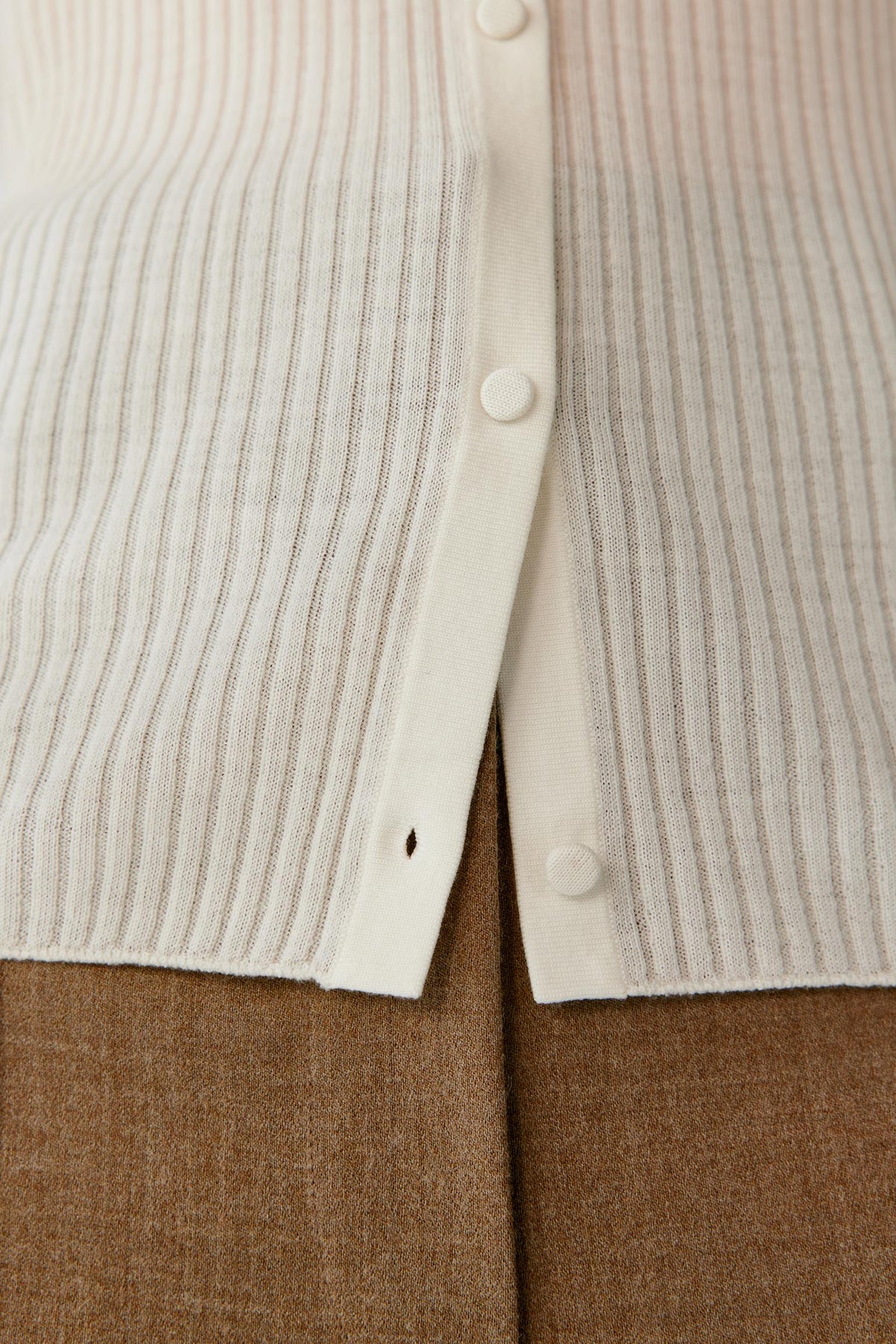 Close-up of a cream ribbed knit cardigan with white buttons, layered over a brown textured garment.