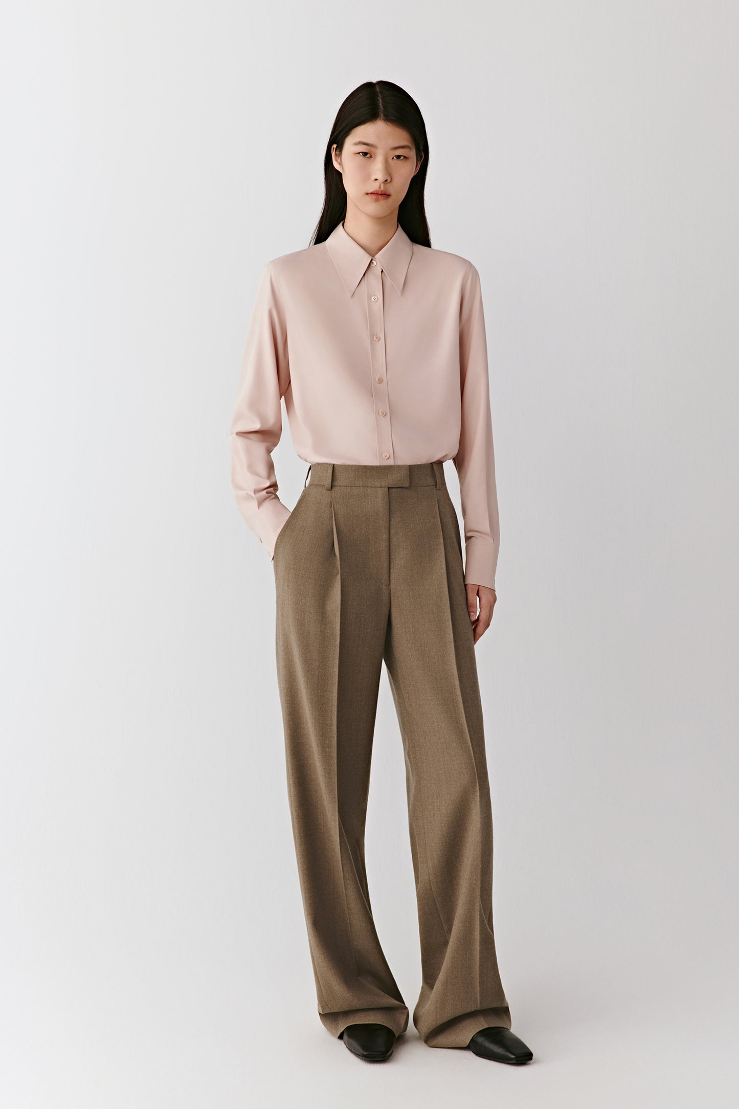 Full-length front view of the model wearing the beige wool flannel trousers with a pale pink top, showing the straight, pressed leg.