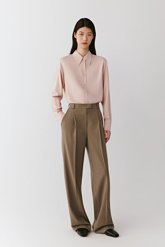 Full-length front view of the model wearing the beige wool flannel trousers with a pale pink top, showing the straight, pressed leg.