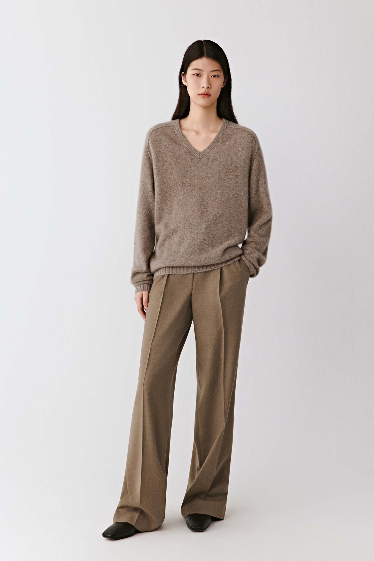 Full-length front view of the model wearing the brown mélange cashmere sweater with wide trousers, showing its relaxed and elegant silhouette.