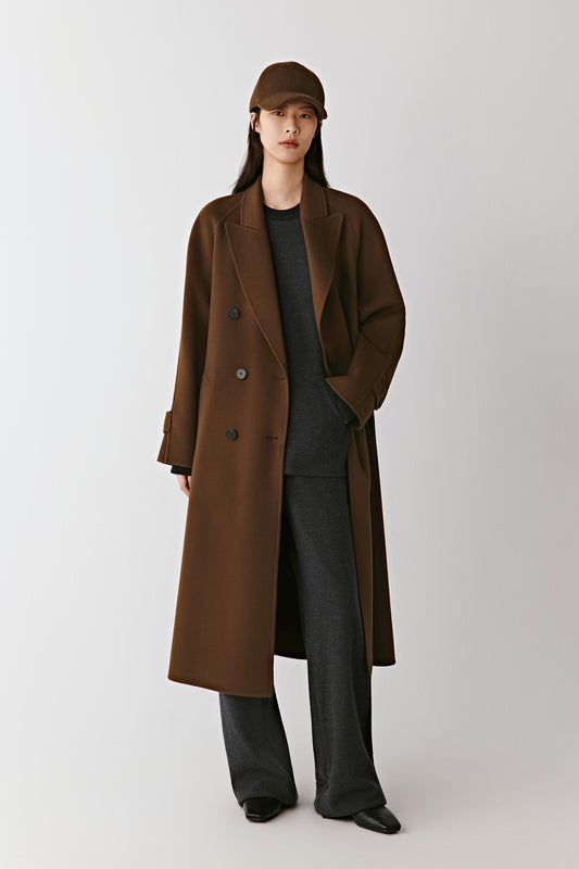 Full-length front view of the model wearing the brown double-faced wool and cashmere coat, showing its long, fluid silhouette and tonal belt.