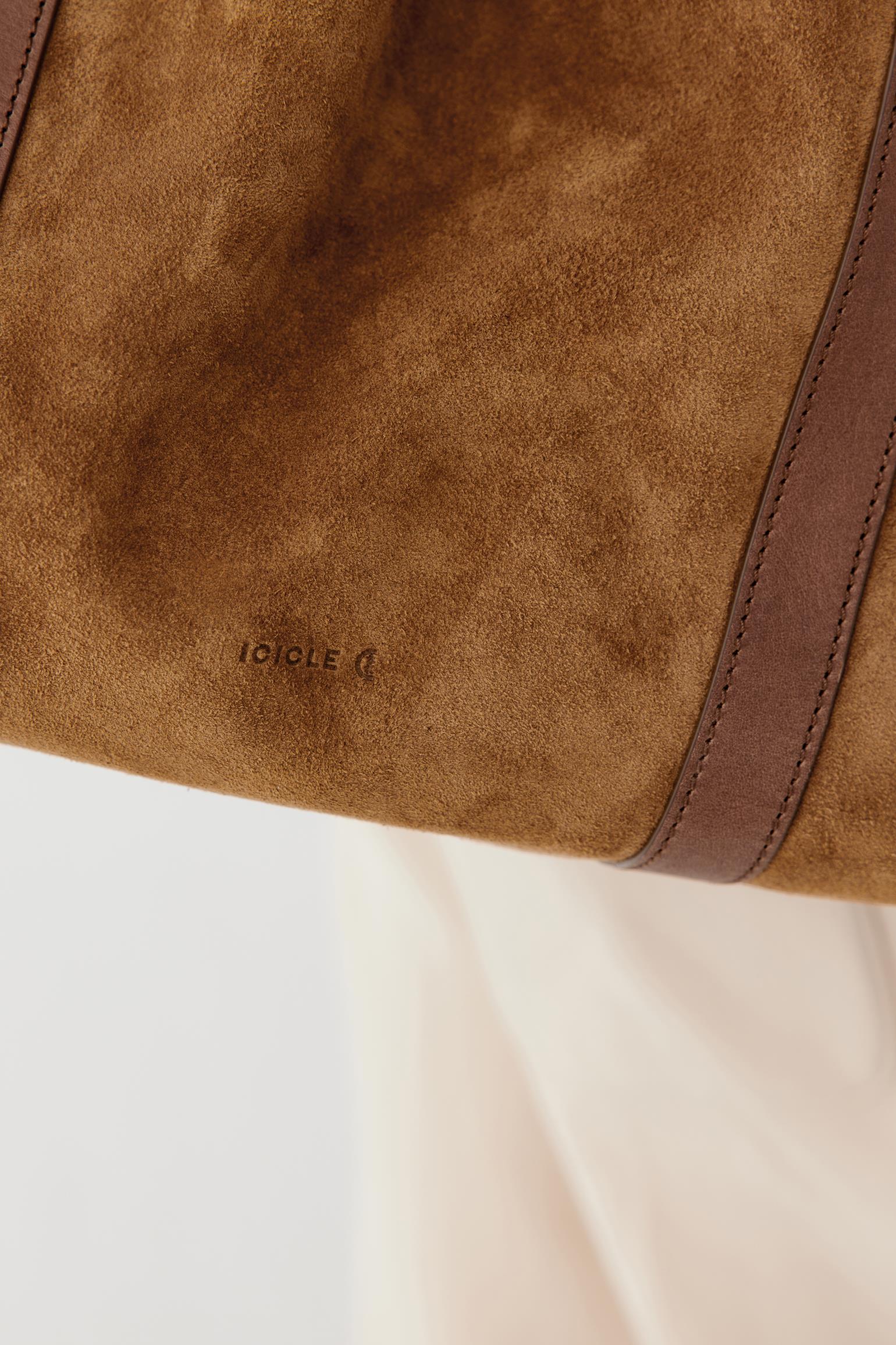 Close-up of a brown suede or suede-like bag surface with a darker brown leather trim strip and a small embossed brand mark reading 'ICICLE'.