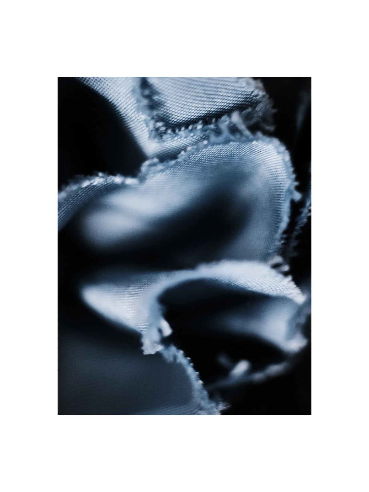 Abstract close-up macro photograph of sculptural raw-edged denim fabric folds, showing the light blue woven textile with frayed selvage edges dramatically draped and twisted against a deep black background, highlighting the texture and weight of the indigo cotton weave. AW26 Icicle Atelier Menswear.