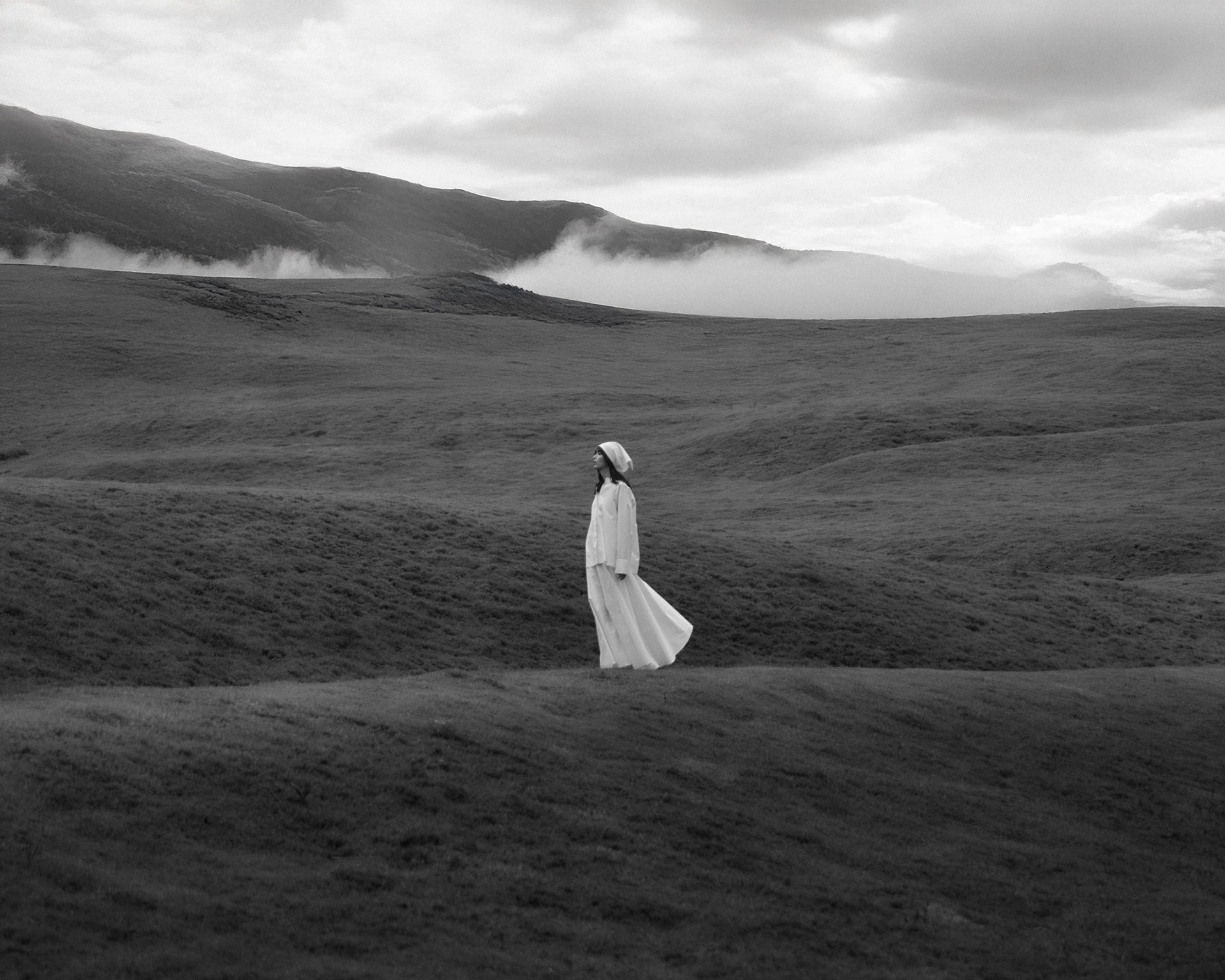 Person wearing a long, flowing white dress in a misty landscape, highlighting fluidity and lightness.