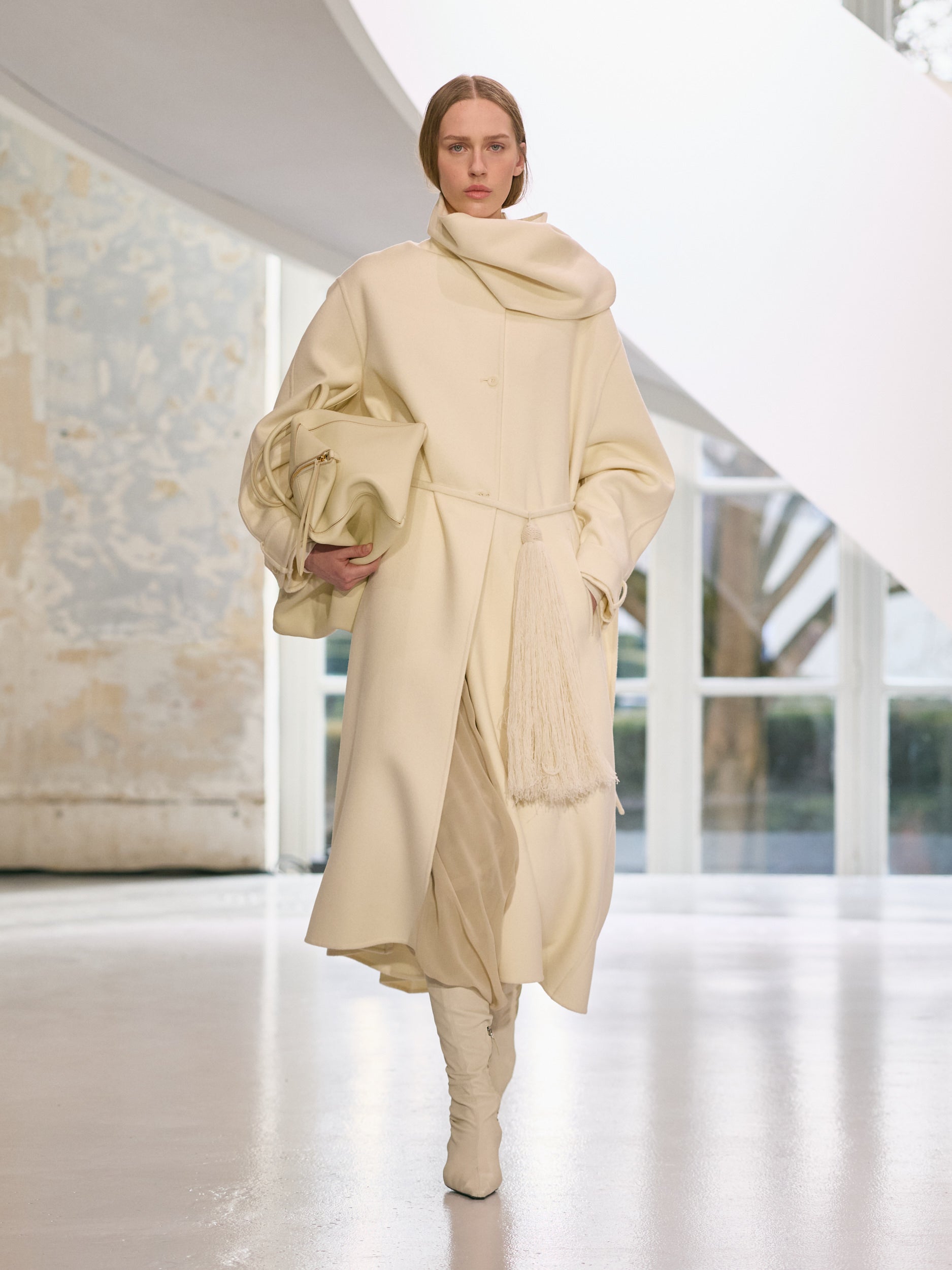 Model wearing a beige outfit walking on a runway.
