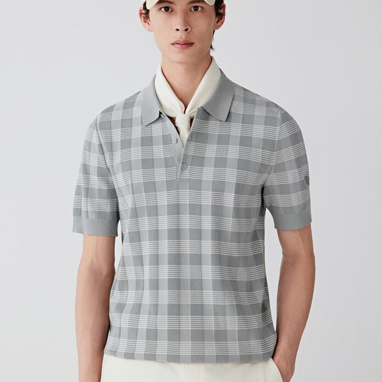Man wearing a light grey cotton knit polo-style pullover with a subtle checked pattern and relaxed straight silhouette, styled with off-white trousers and a cap. He turns and shifts between front, side and three-quarter views, revealing the lightweight, breathable cotton knit and its soft, fluid drape. The polo collar, short button placket and clean sleeve finishes remain consistently visible, while the fabric moves naturally with the body, showing ease through the shoulders and torso, and a balanced, non-r