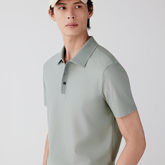 Man wearing a light grey cotton and silk jersey polo shirt with a relaxed, straight cut, styled with off-white trousers. He moves between front and angled views, showing the lightweight knit, soft drape and natural stretch of the fabric. The classic collar, short button placket and clean sleeve finish remain visible, while the material subtly follows the body, emphasizing comfort and ease of movement.